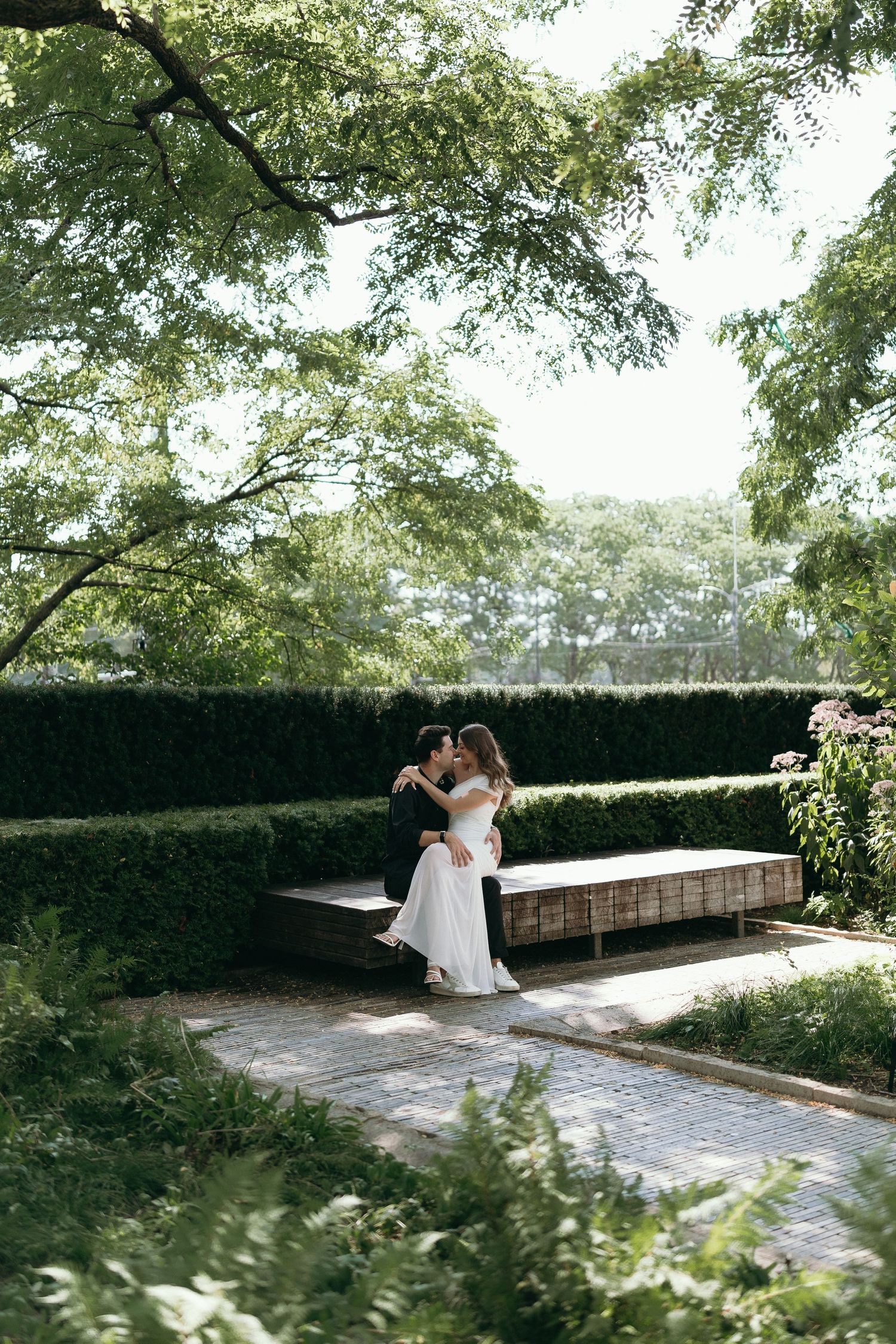 A couple shares an intimate moment on a stone bench in a lush Lurie Garden in Chicago setting surrounded by manicured hedges and trees.