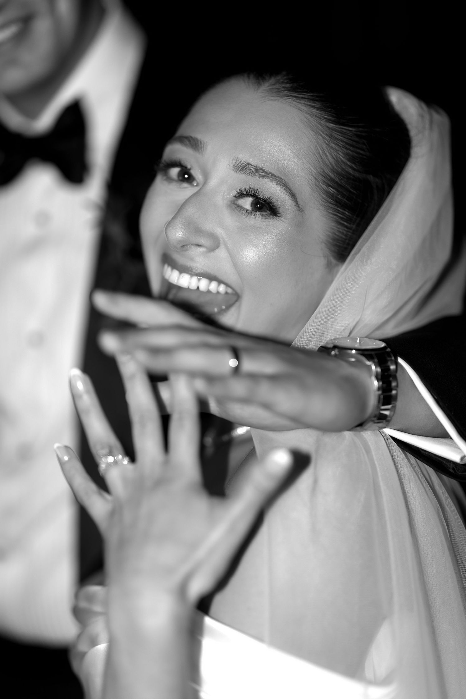 Black and white photo of a joyful bride in veil showing her wedding ring, smiling radiantly on her wedding day.