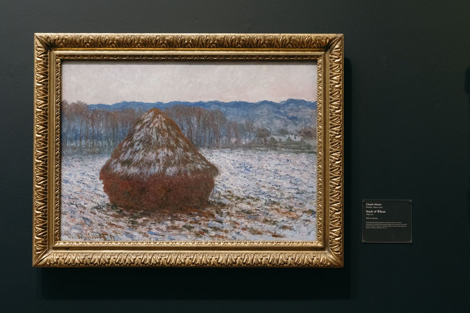Framed Monet haystack painting displayed on dark museum wall.