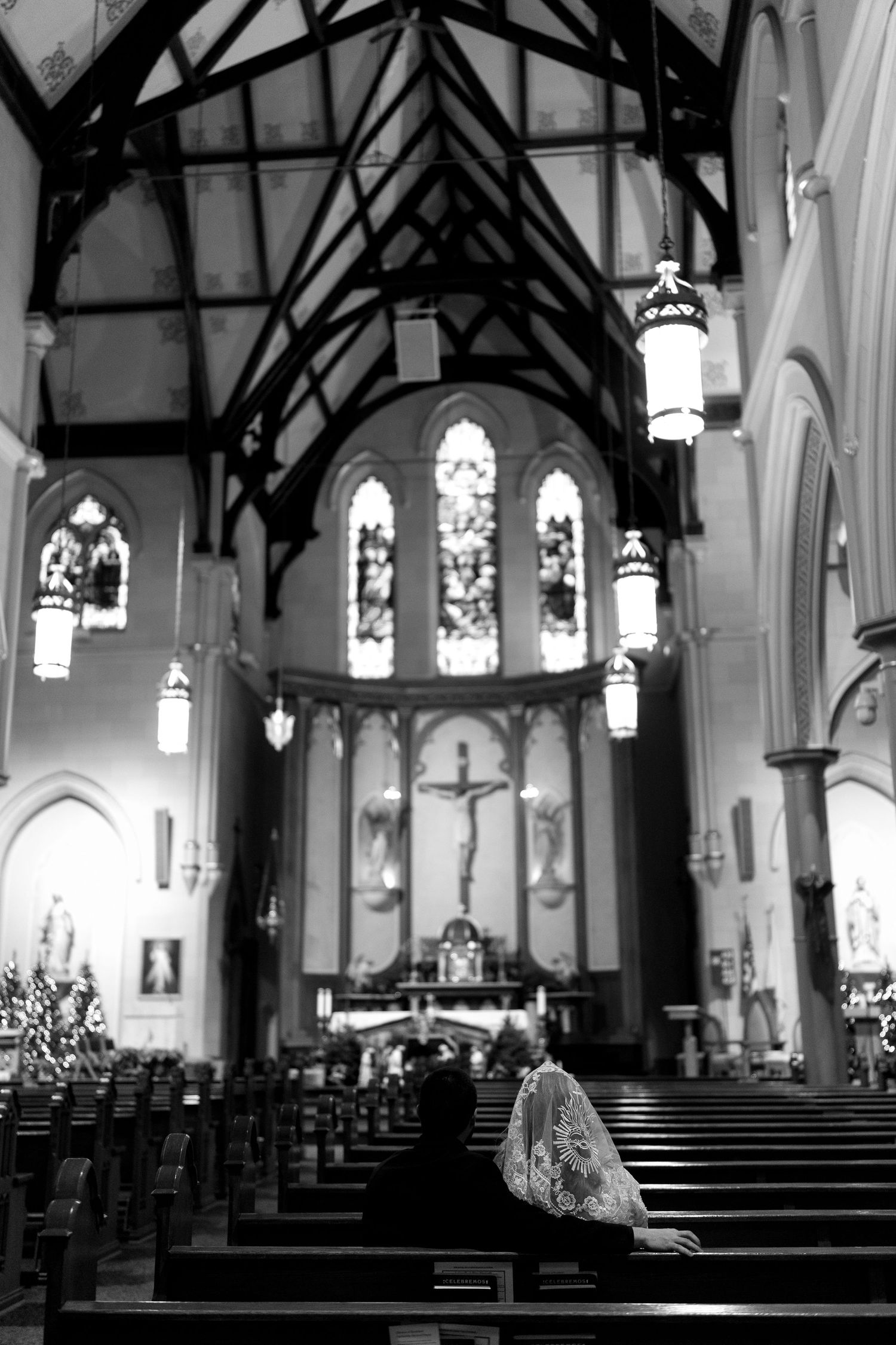 A gothic church interior with vaulted ceilings, stained glass windows and hanging lanterns in black and white.