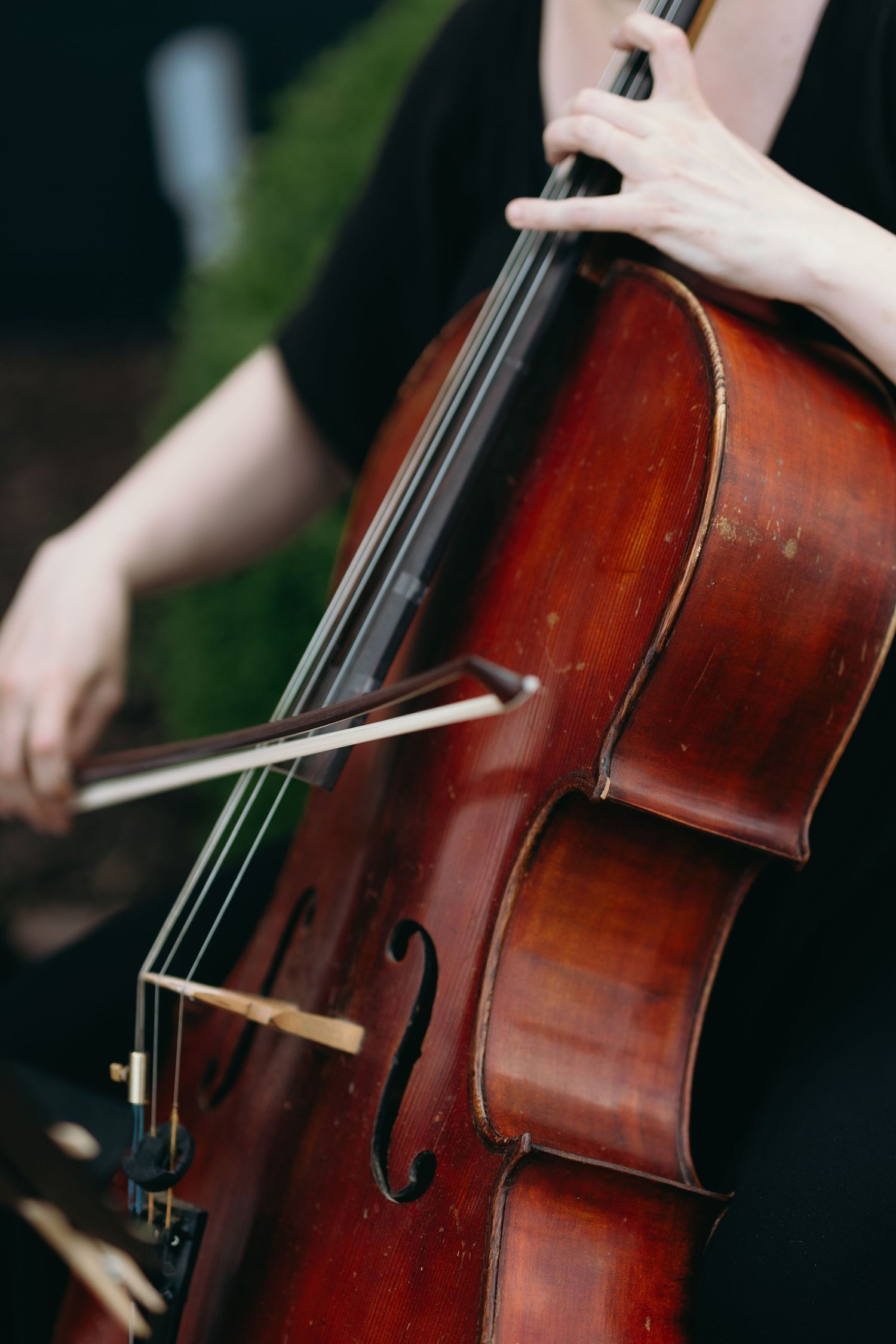 Close-up of musician playing a rich brown cello with bow against dark background.