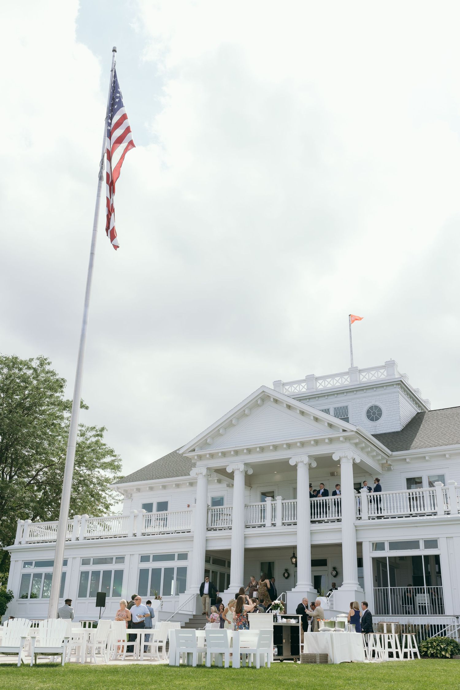 Elegant white country club venue with American flag and guests gathered on the lawn for an outdoor event. The Waters OshKosh