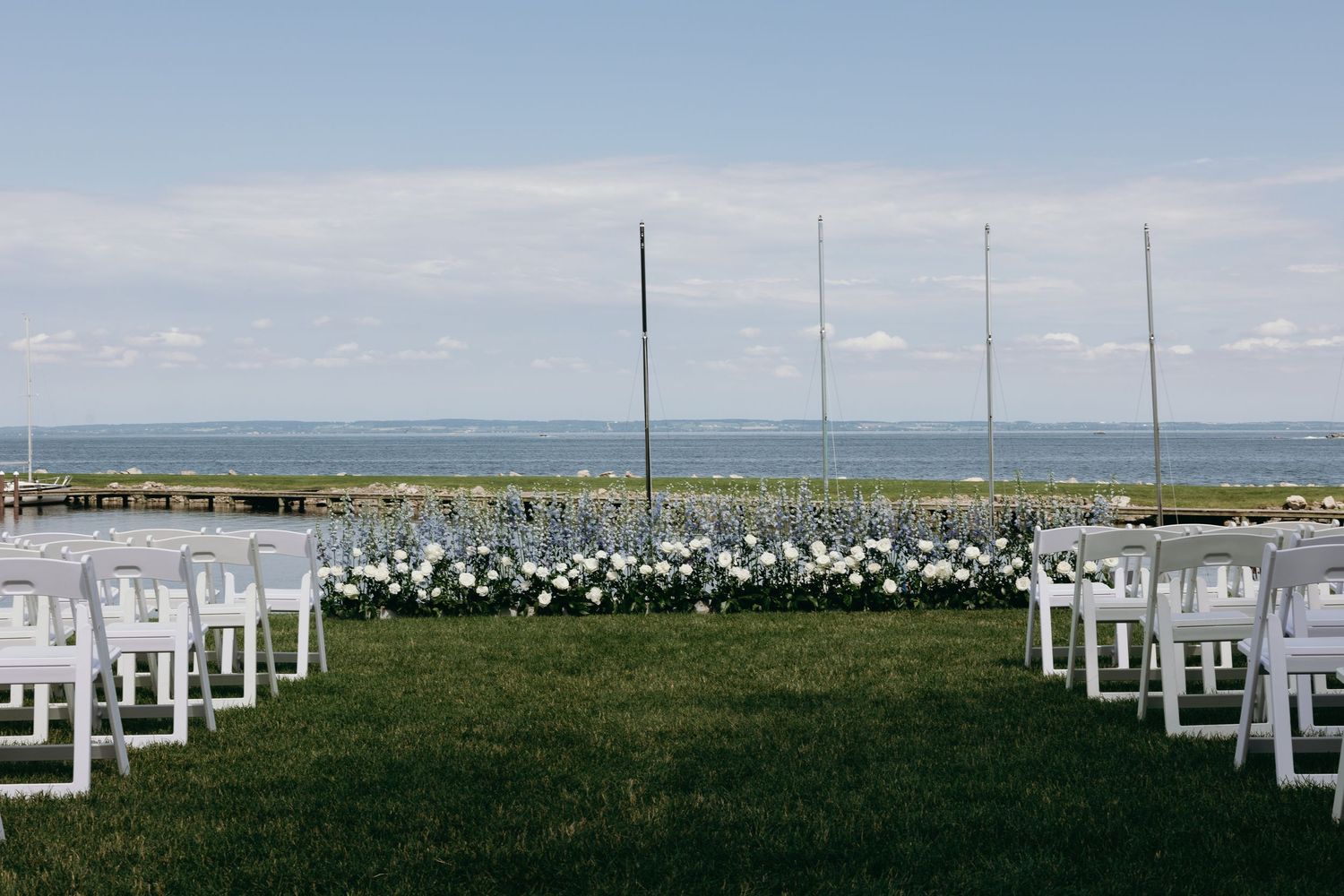 White wooden chairs arranged in rows facing the ocean for an outdoor waterfront wedding ceremony setup.