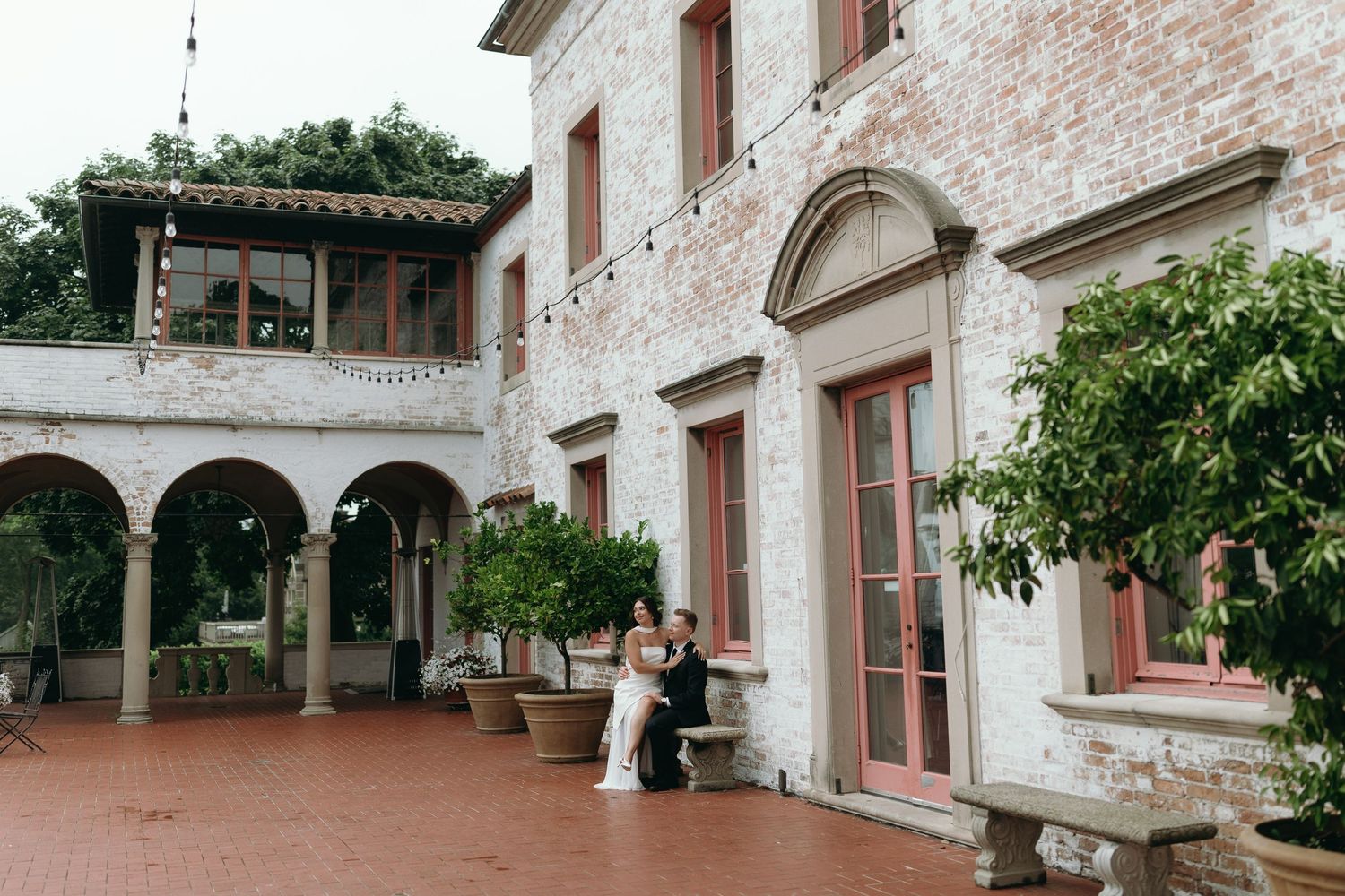 A couple embraces on a terrace of a rustic Italian-style villa with arched columns and terra cotta flooring. The Villa Terrace in Milwaukee
