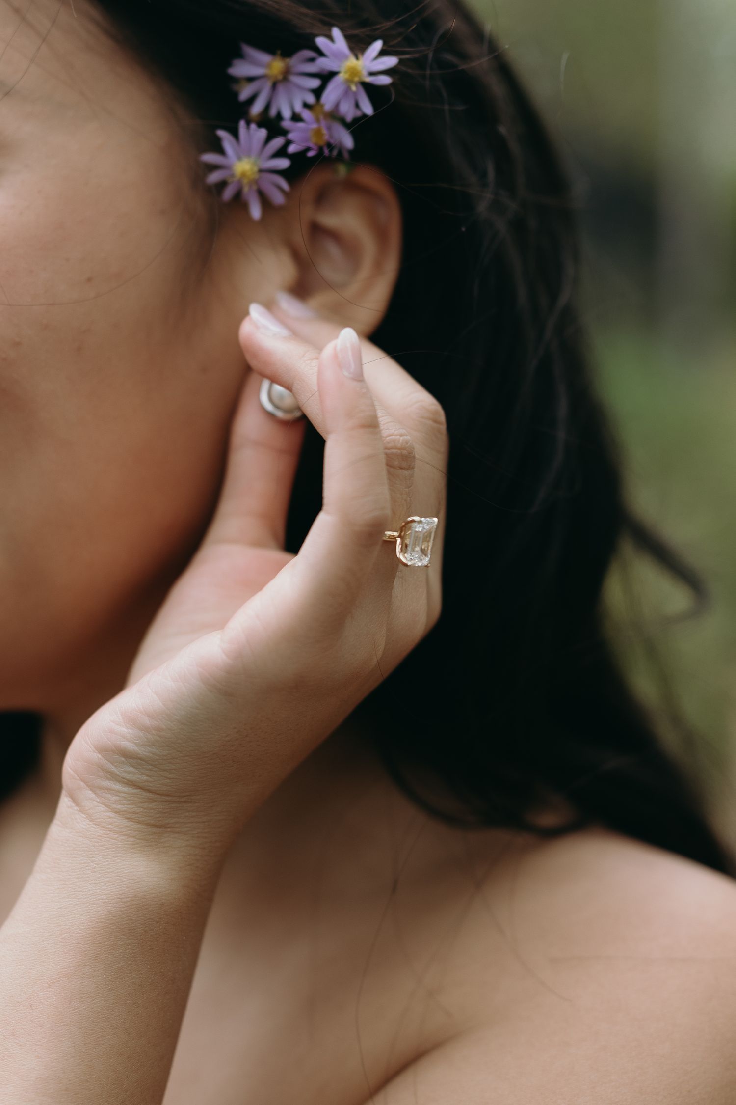 Close-up of delicate purple daisies in hair and a sparkling ring on display.
