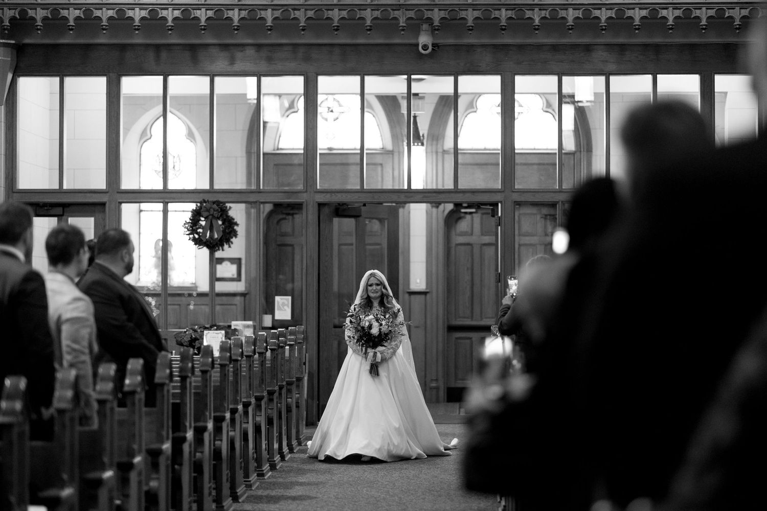 Black and white photo of a bride walking down the church aisle during a traditional ceremony.