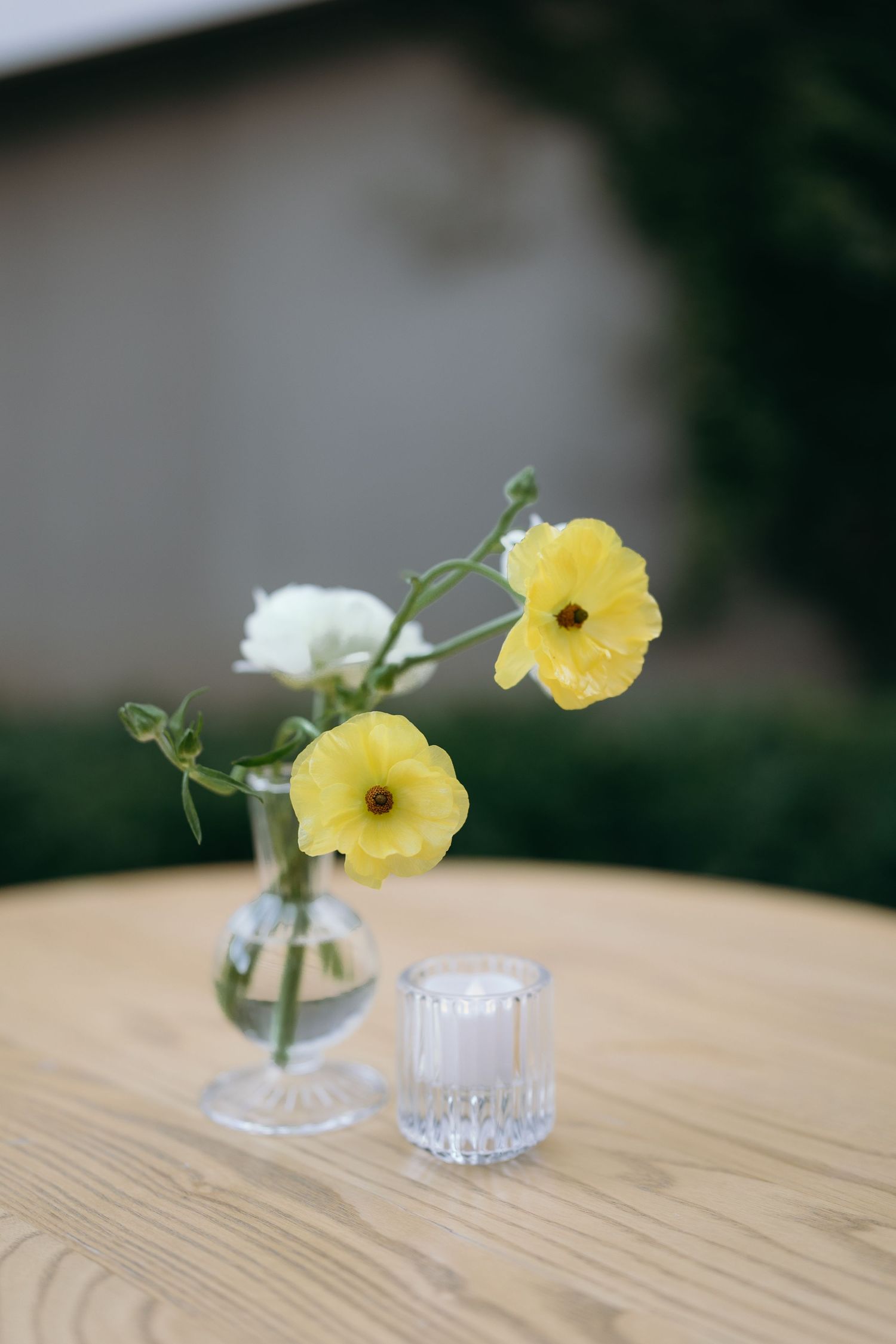 Yellow and white flowers in small glass vase on wooden table with crystal glass.