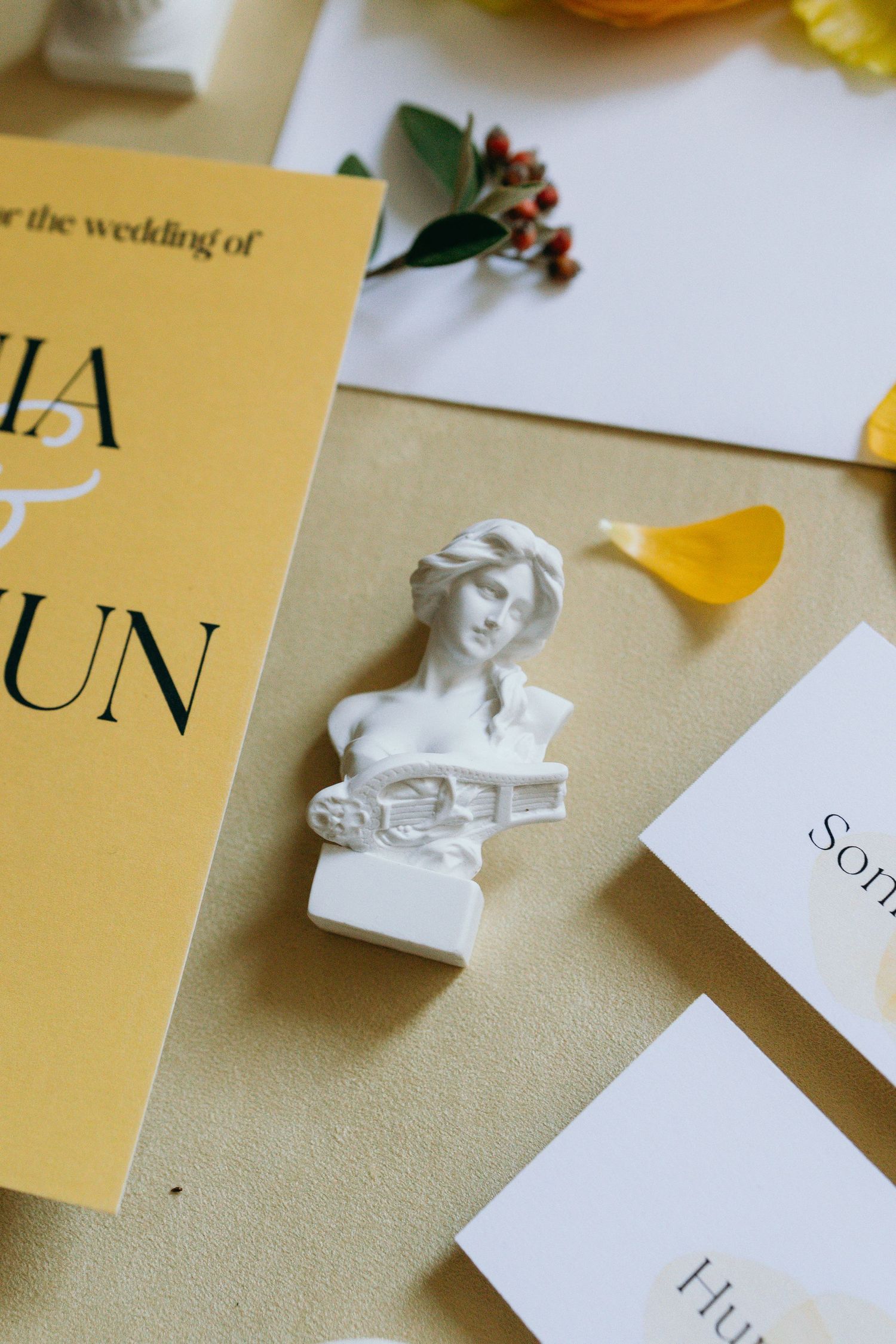 Wedding invitation with gold text and decorative white bust statue on beige background.