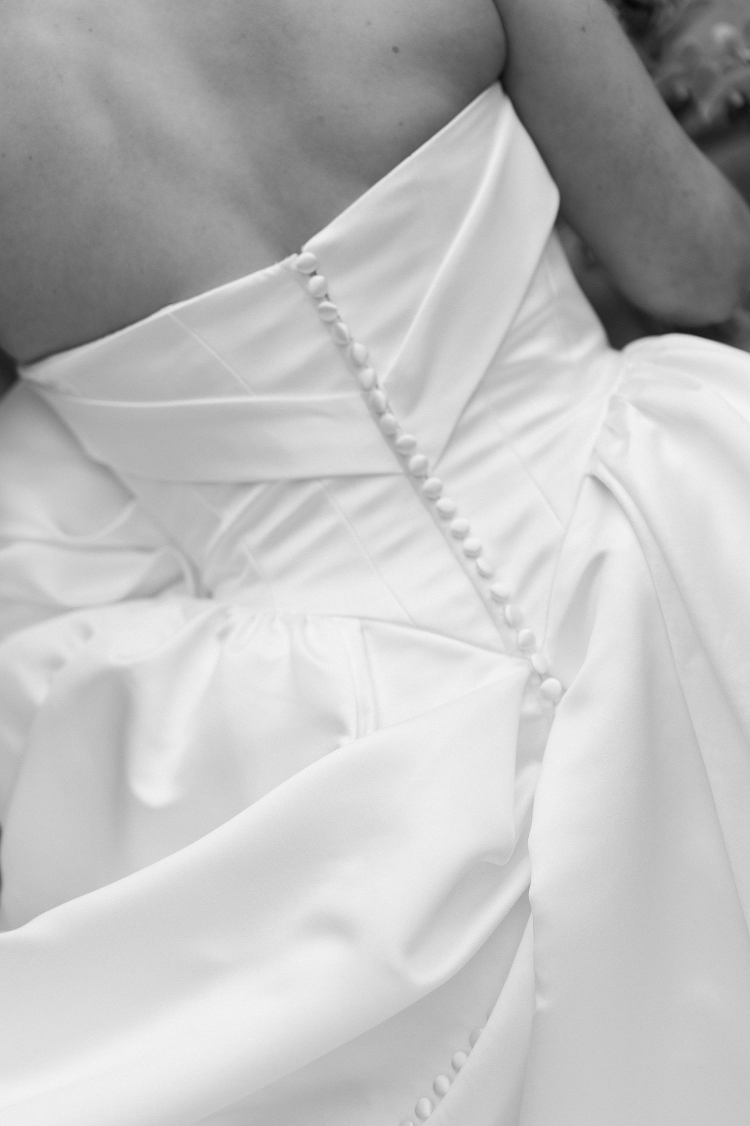 Close-up detail of a white wedding dress showing delicate button closures and pleated fabric along the back.