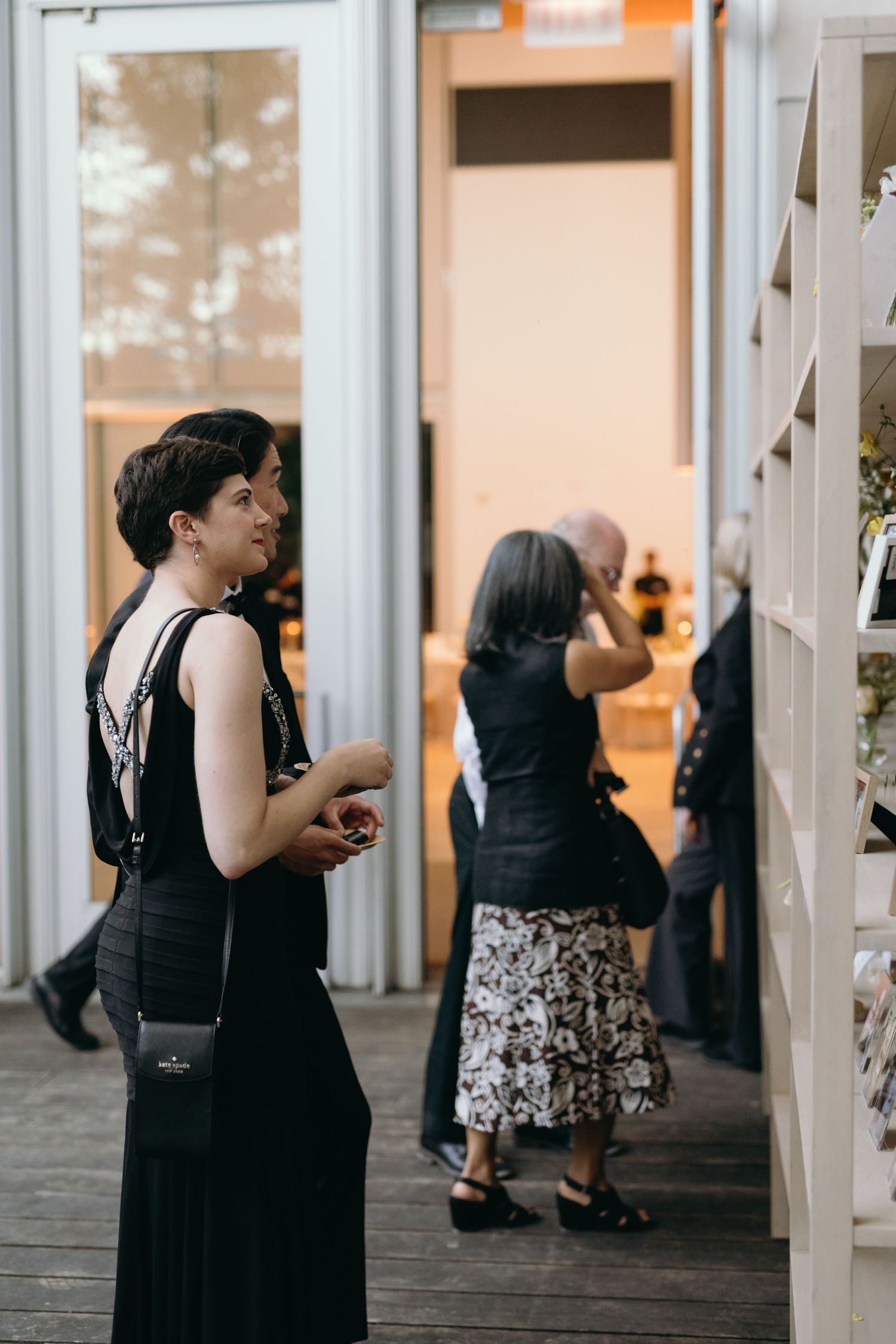 Party guests in elegant black dresses gather on a deck during an evening event.
