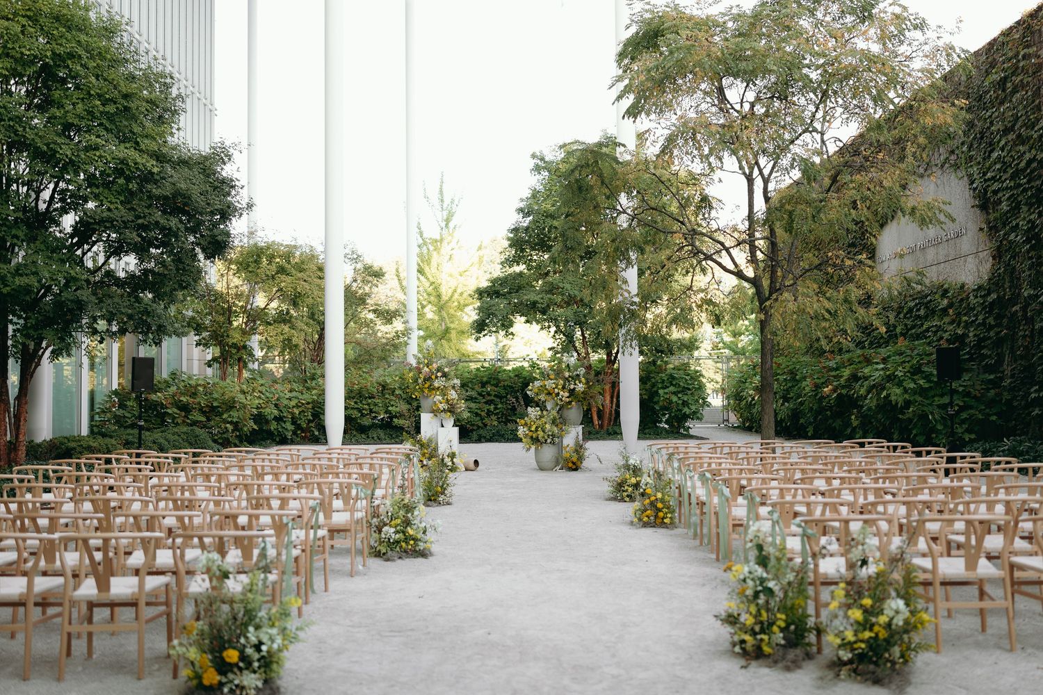 Outdoor wedding ceremony setup with rows of wooden chairs and floral decorations along the aisle.