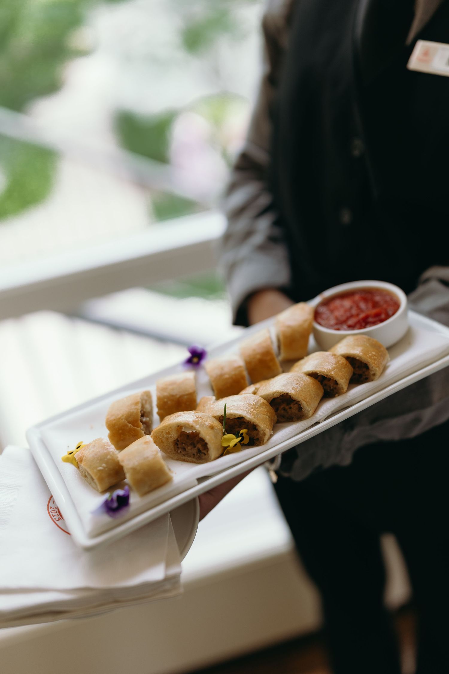Platter of rolled appetizers served with red dipping sauce on a white plate.