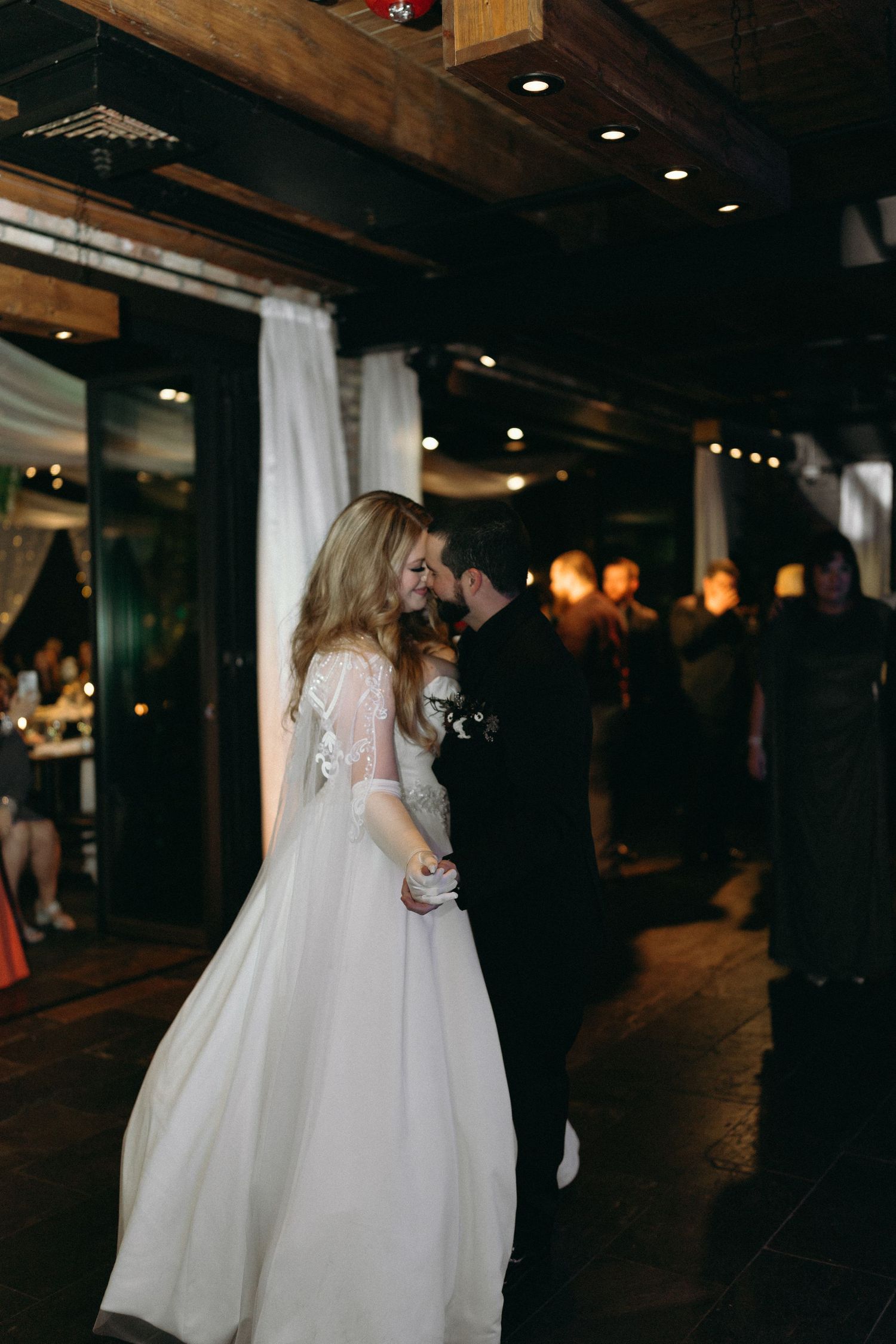 Couple sharing intimate dance moment at wedding reception in rustic venue with exposed beams.
