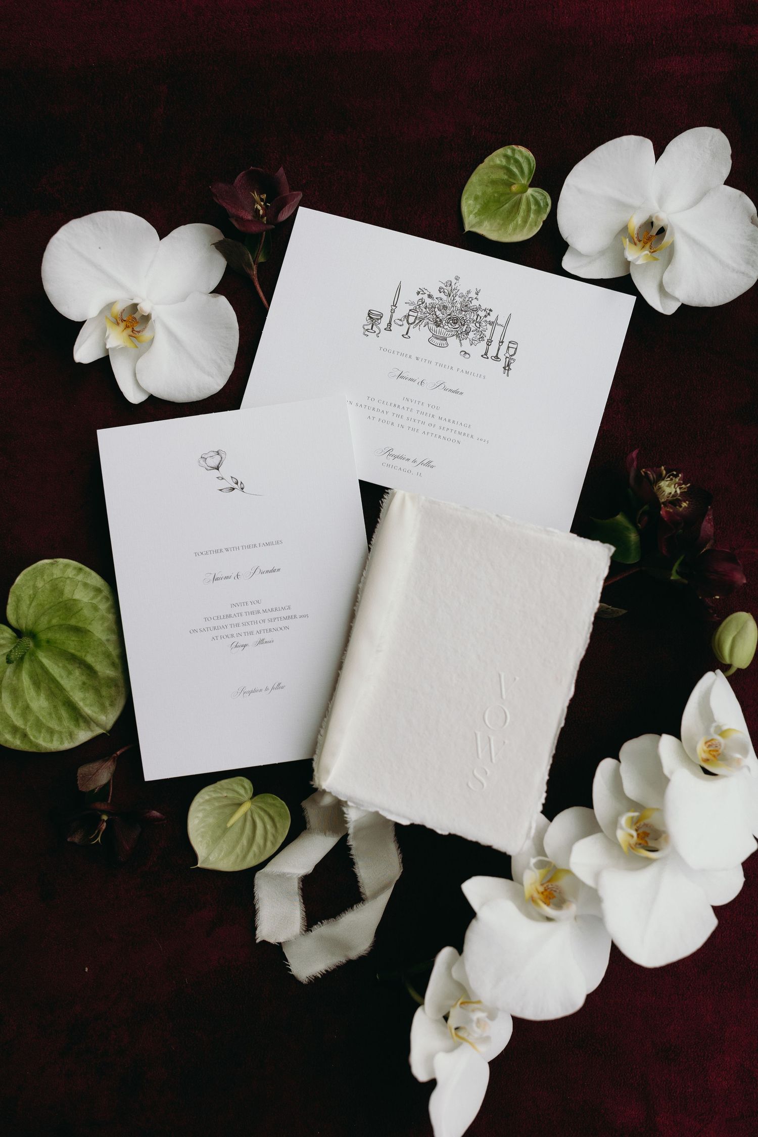 White wedding invitations with elegant calligraphy displayed with delicate orchid flowers and green leaves on dark background.