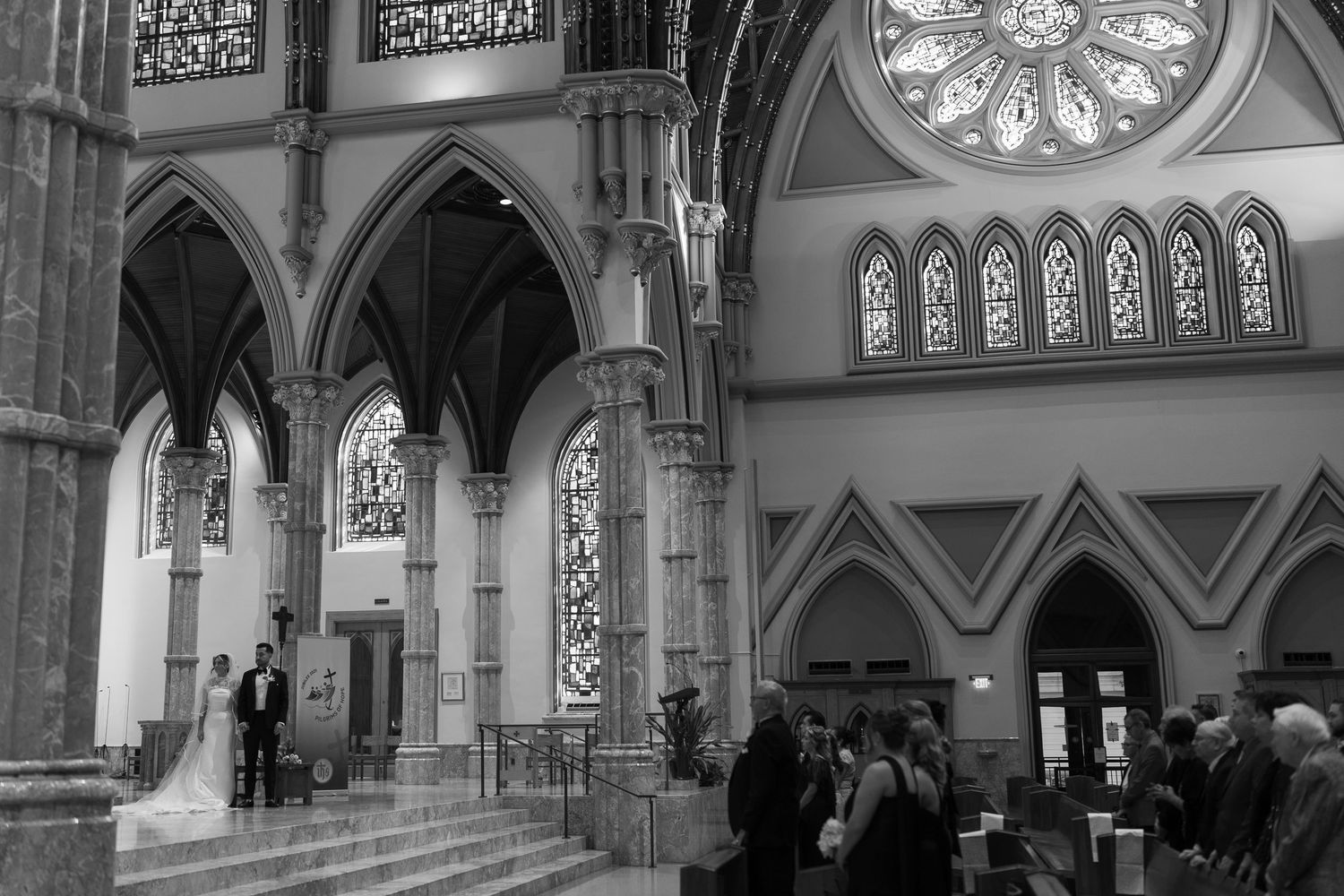 Interior view of a gothic church sanctuary with ornate stained glass windows, arches, and decorative architectural details.