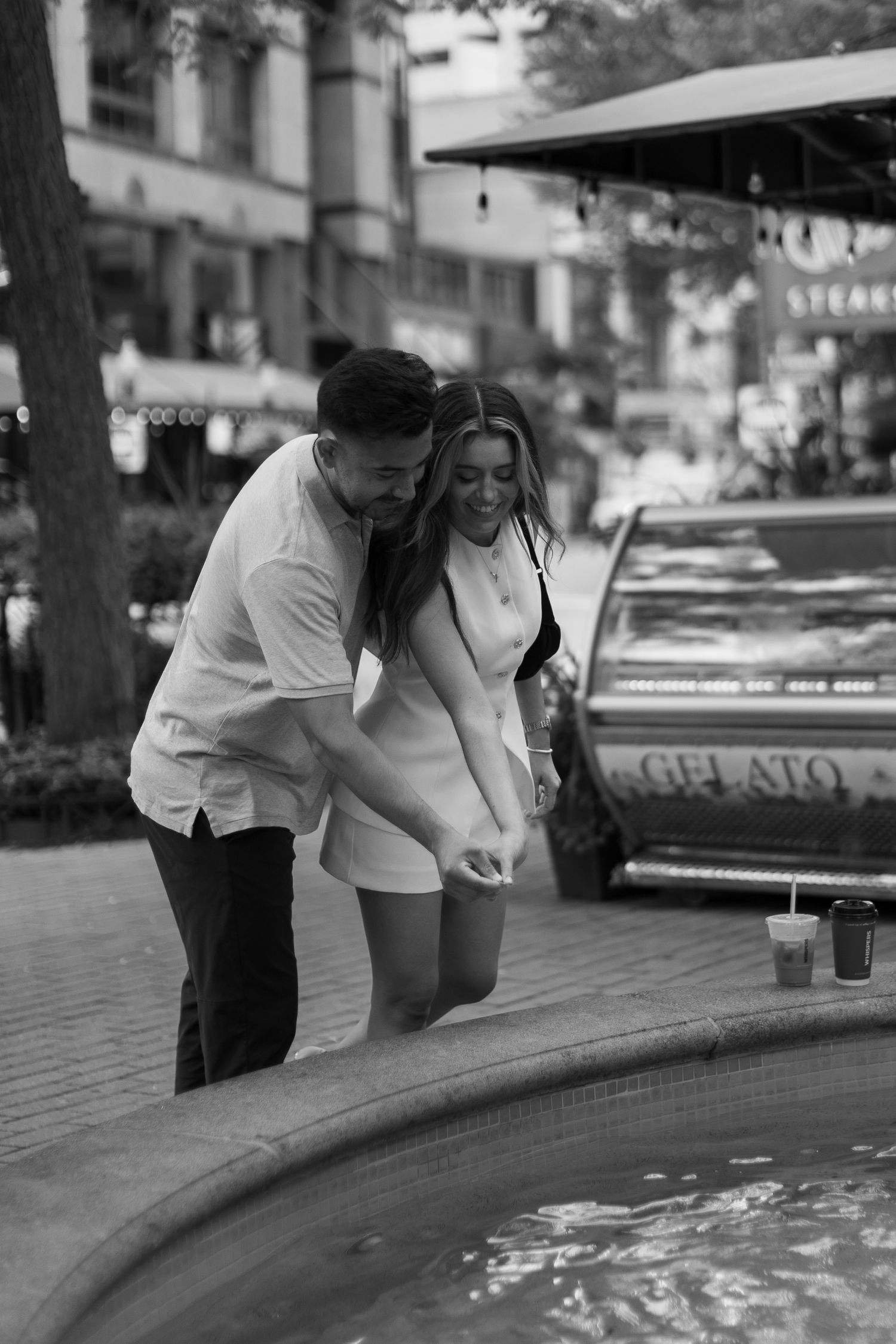 A couple in white outfits leans over a reflecting pool or fountain edge while holding beverages, shown in multiple frames.