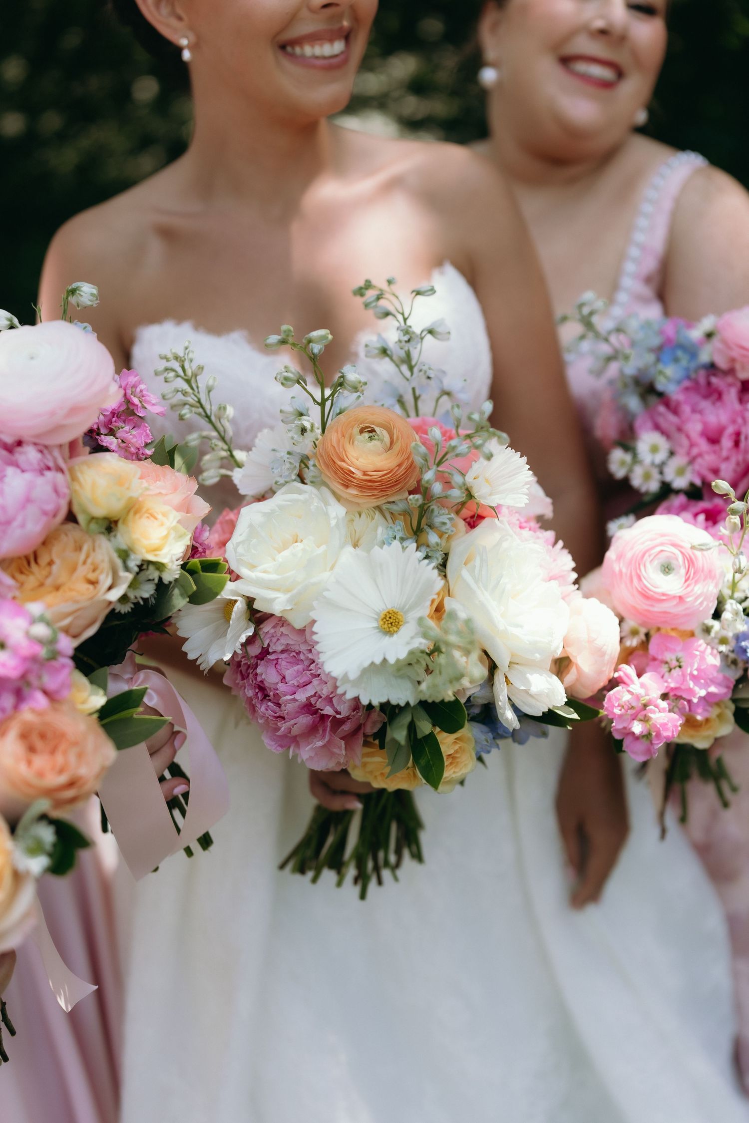 Bride and bridesmaids holding lush pink, white, and peach wedding bouquets with ranunculus and peonies.