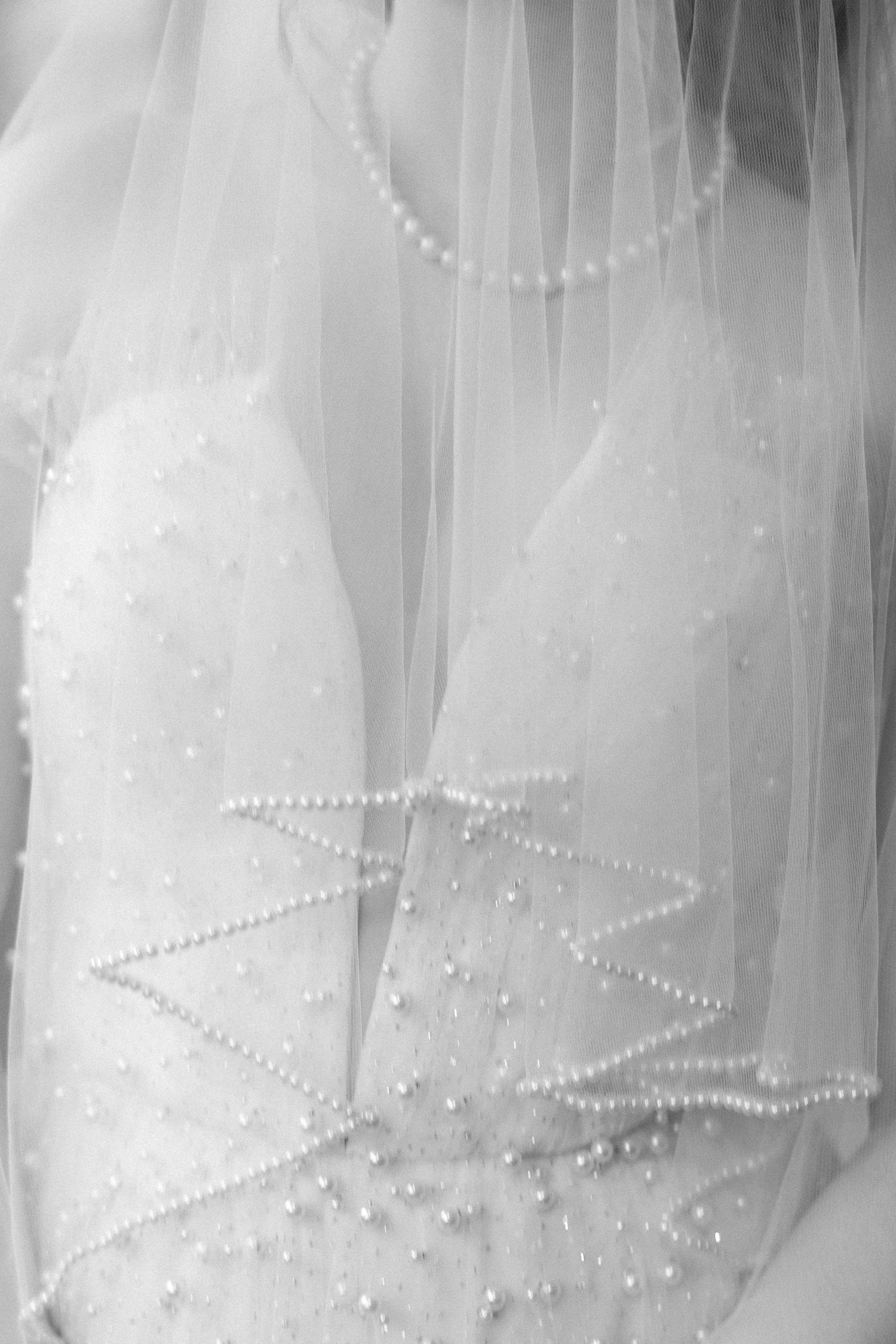 Close-up black and white photo of a bridal gown with pearl embellishments and flowing tulle veil.
