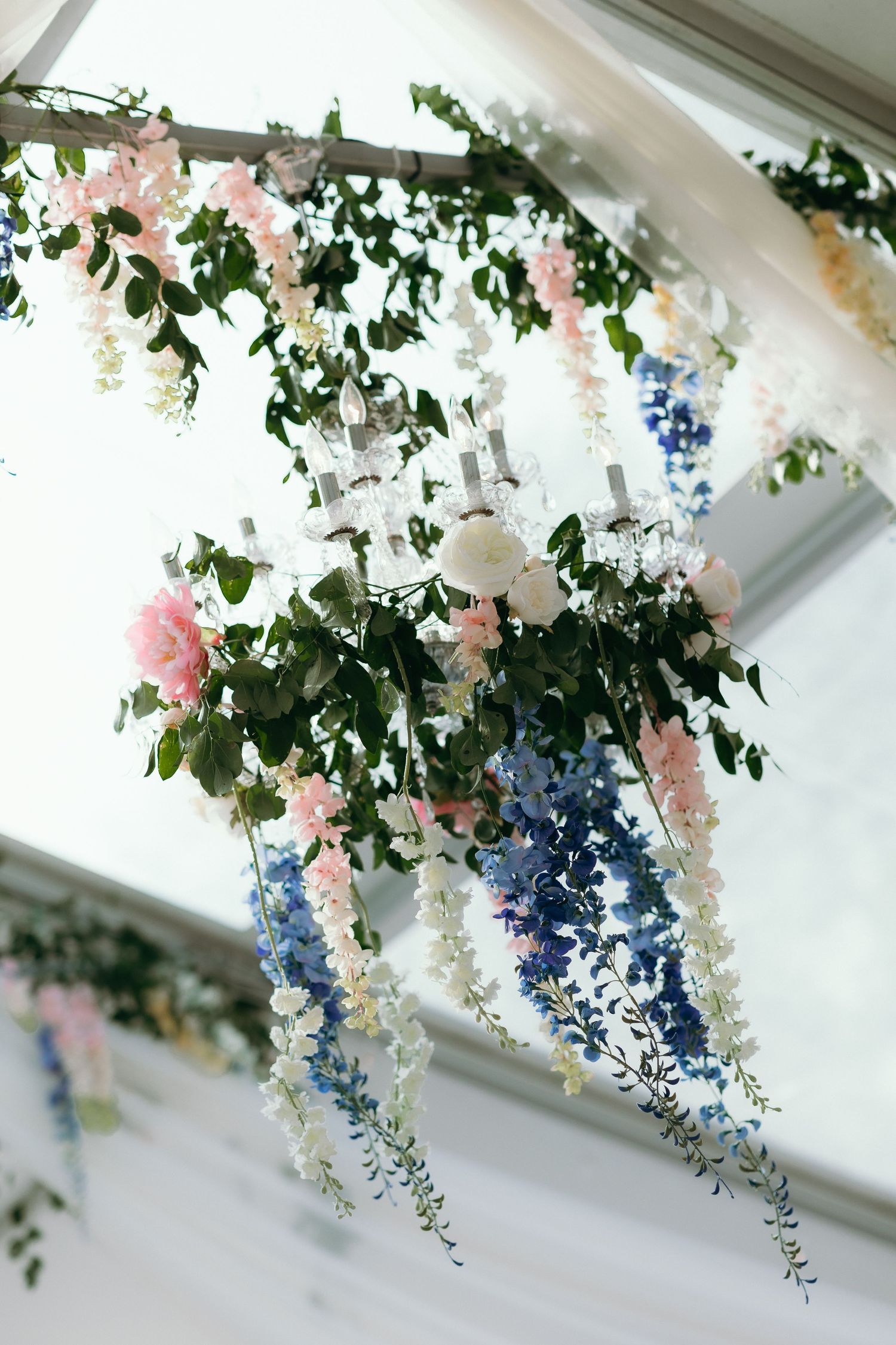 Elegant wedding chandelier adorned with cascading pink, blue, and white flowers with lush greenery.