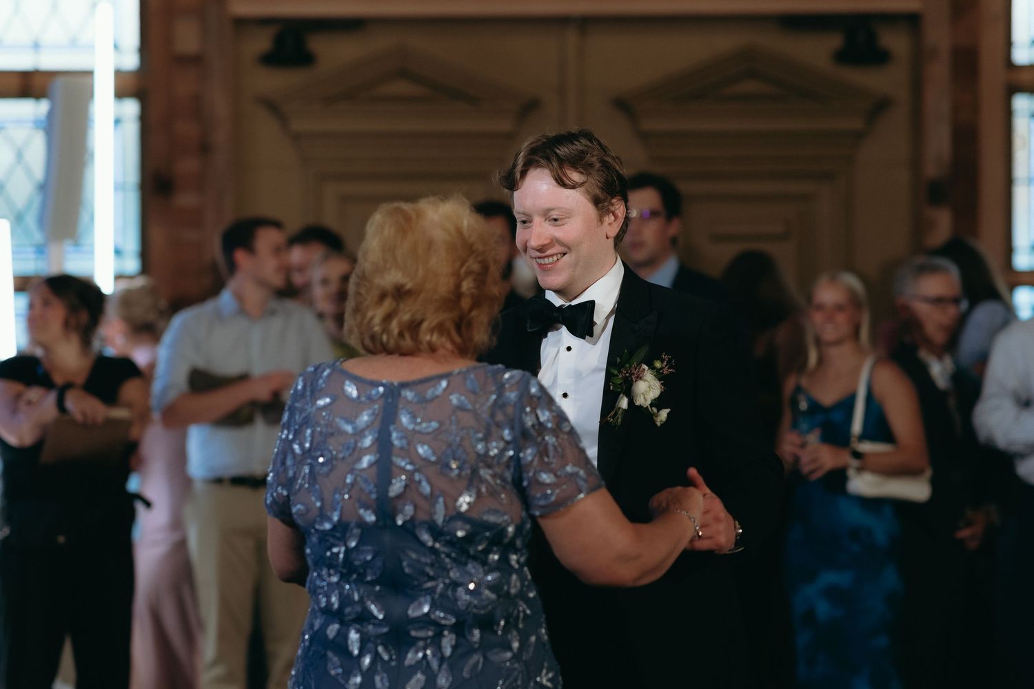 Groom in tuxedo sharing mother-son dance at elegant indoor wedding reception.