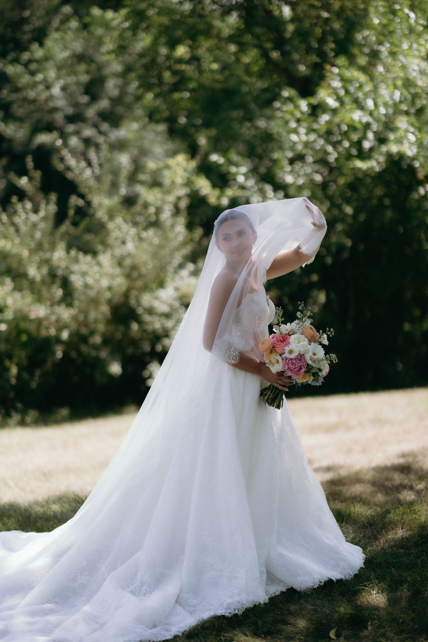 Bride in white ball gown and veil holding colorful bouquet outdoors in lush green garden on wedding day.