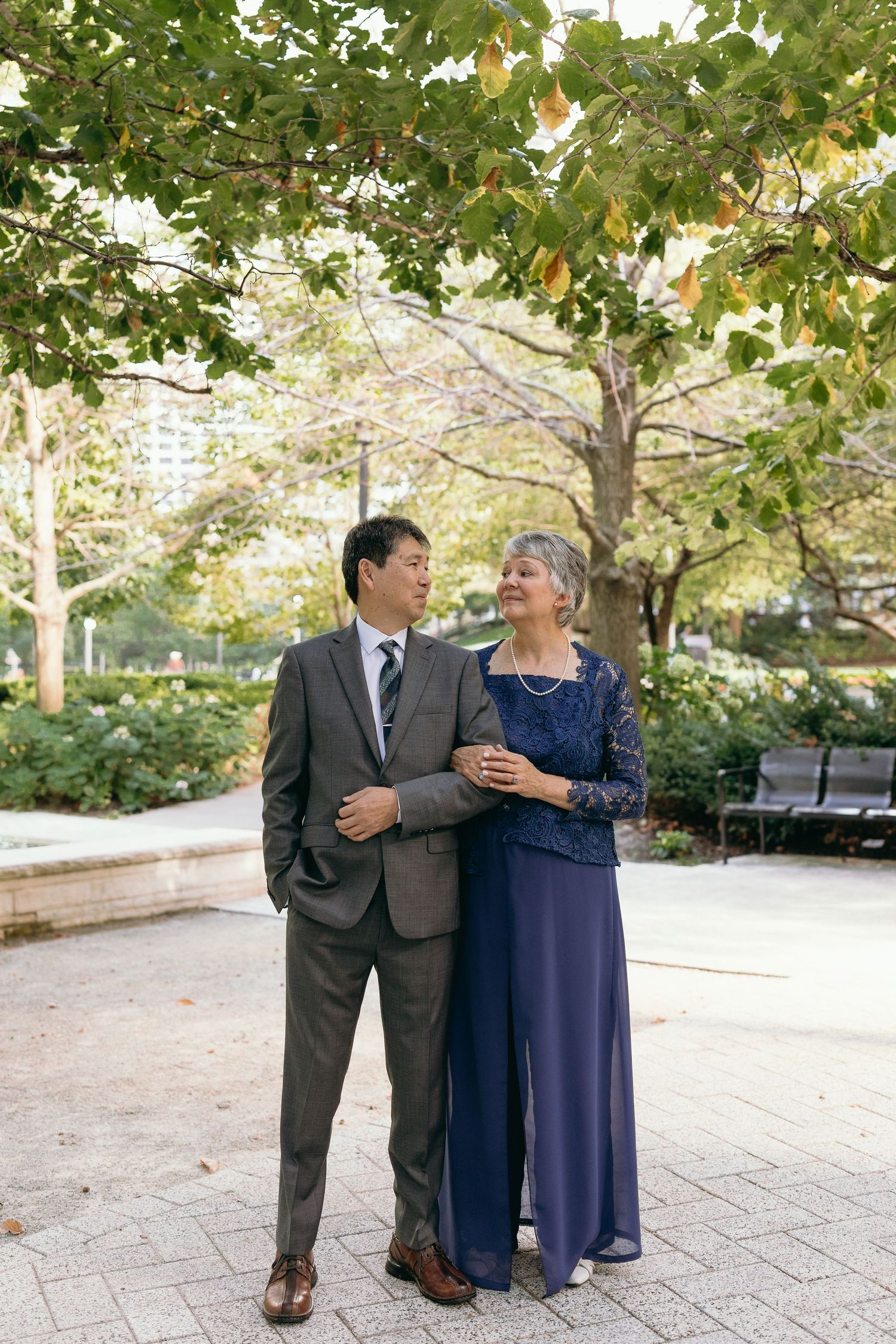 Joyful outdoor portrait of wedding guests sharing laughs in formal attire under green trees.