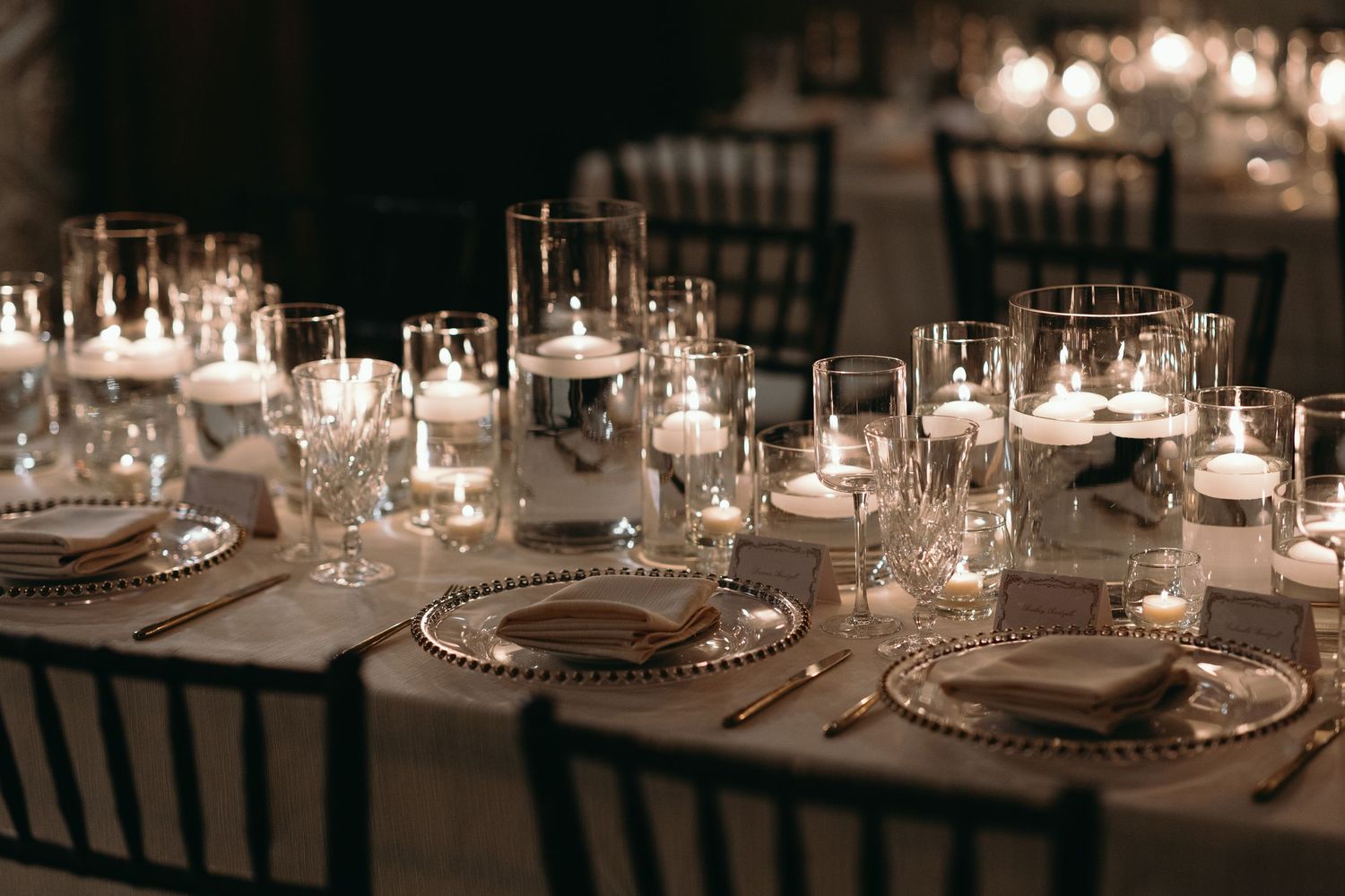 An elegant wedding reception table set with crystal glassware, candles and formal place settings.