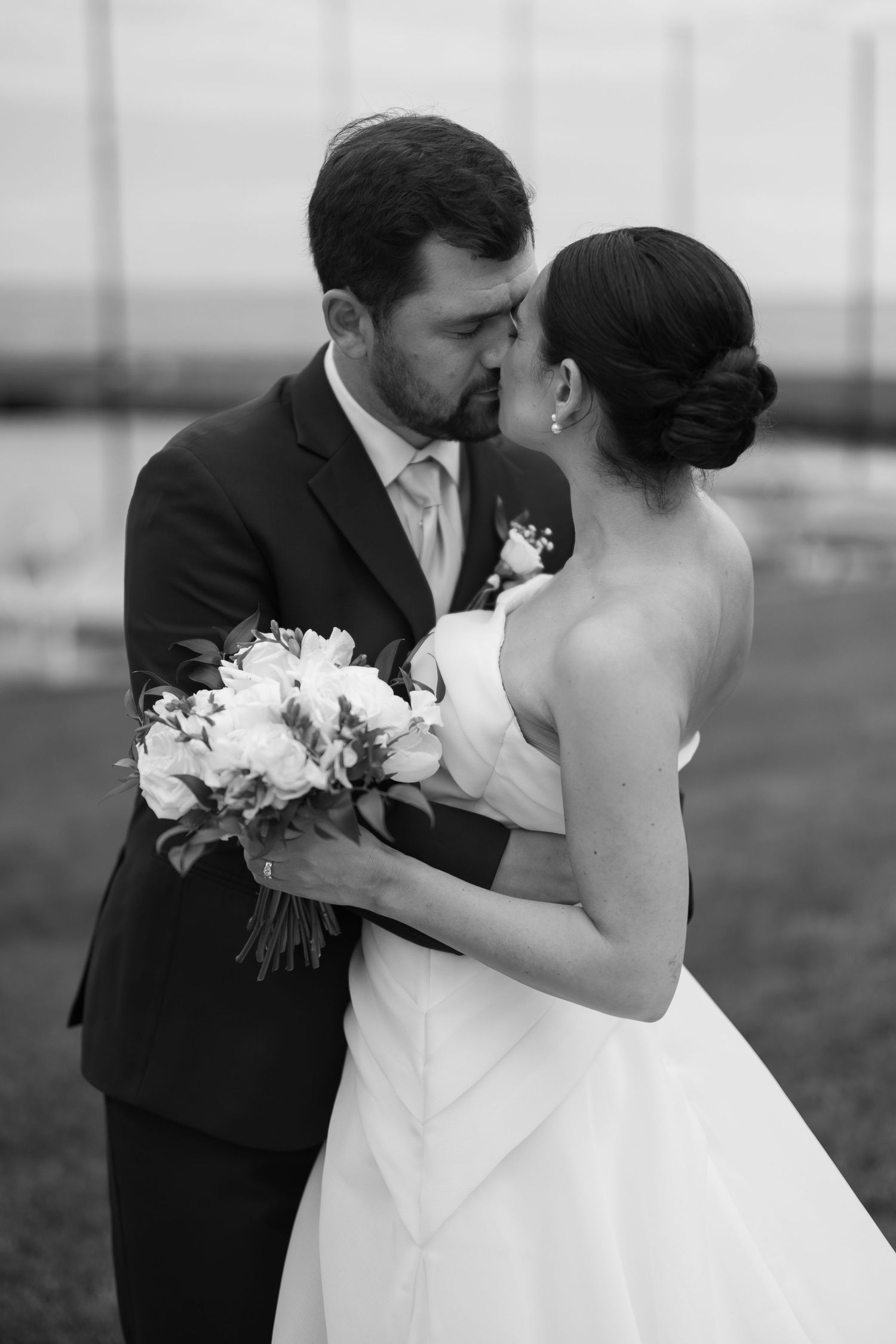 Black and white wedding photo showing couple sharing intimate moment while bride holds elegant white floral bouquet.