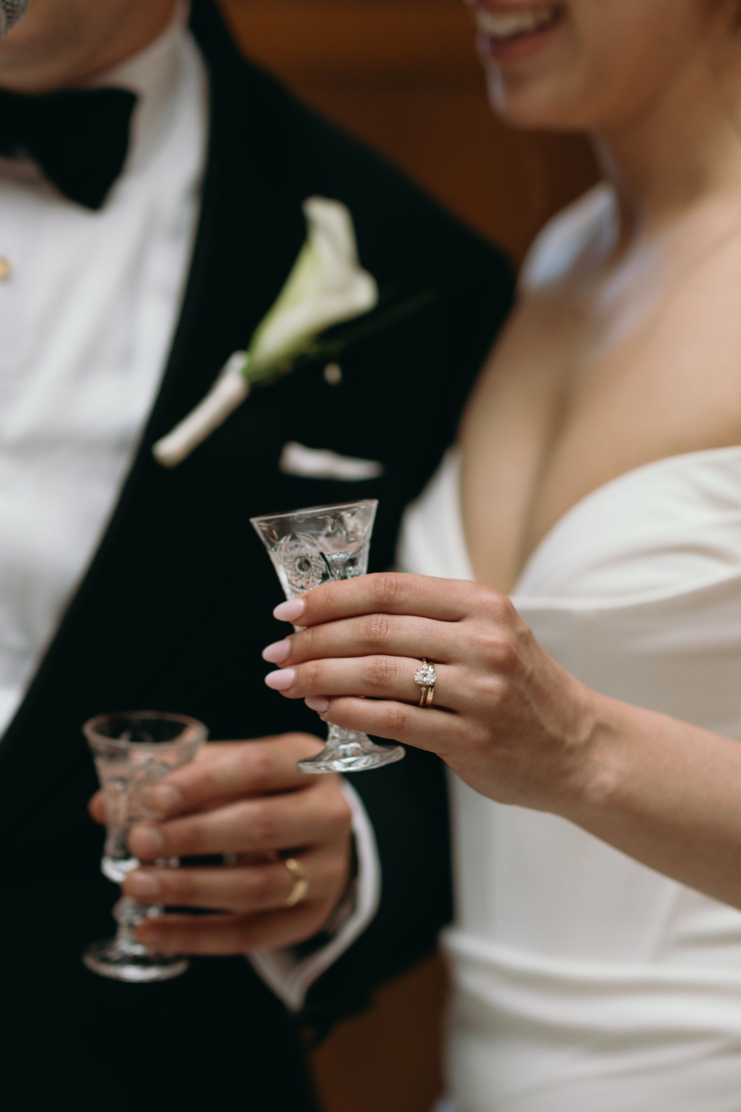 Elegant wedding toast detail with crystal glasses and a white calla lily boutonniere.