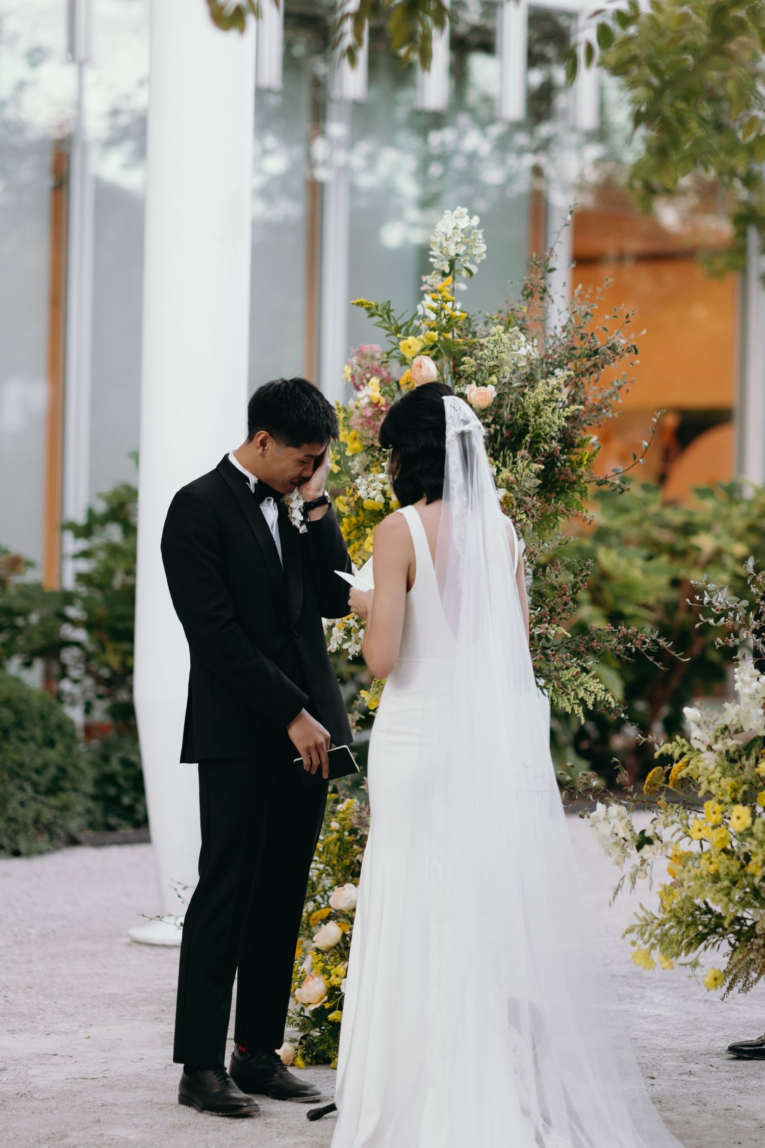 A couple stands together during their wedding ceremony surrounded by yellow and white flowers.