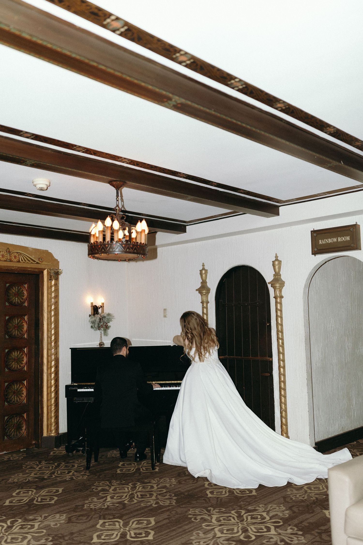 Wedding dress train flowing across vintage room with wooden beams and grand piano.
