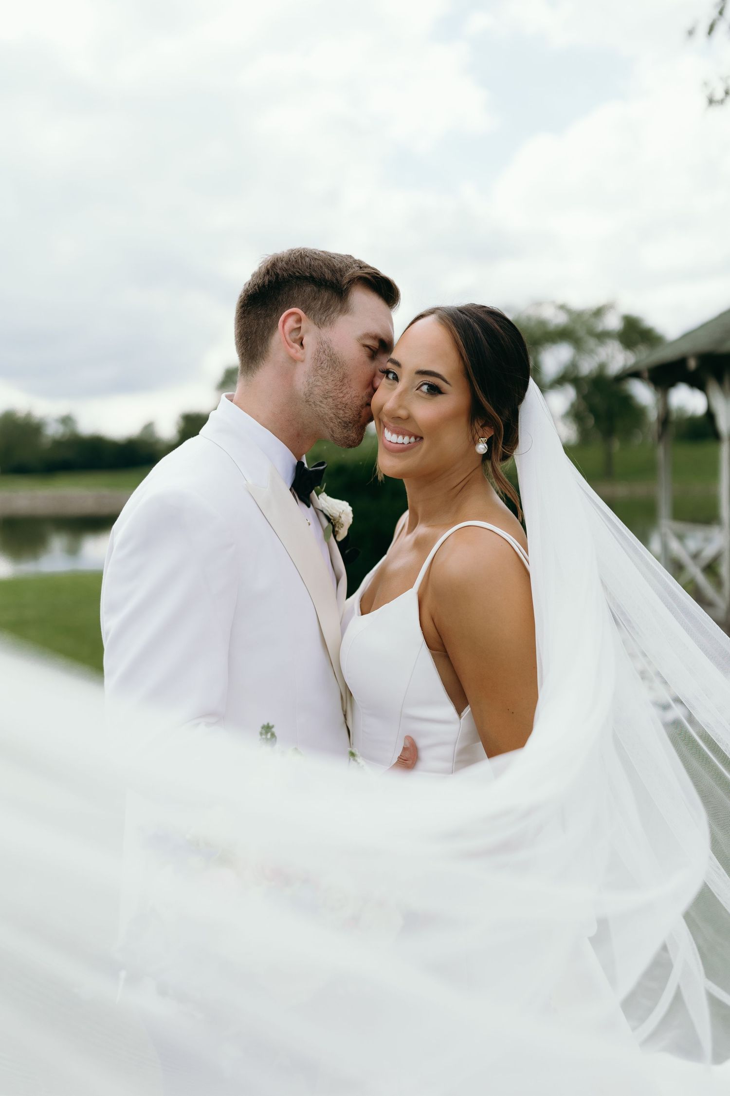 Romantic wedding portrait with flowing veil against cloudy sky.