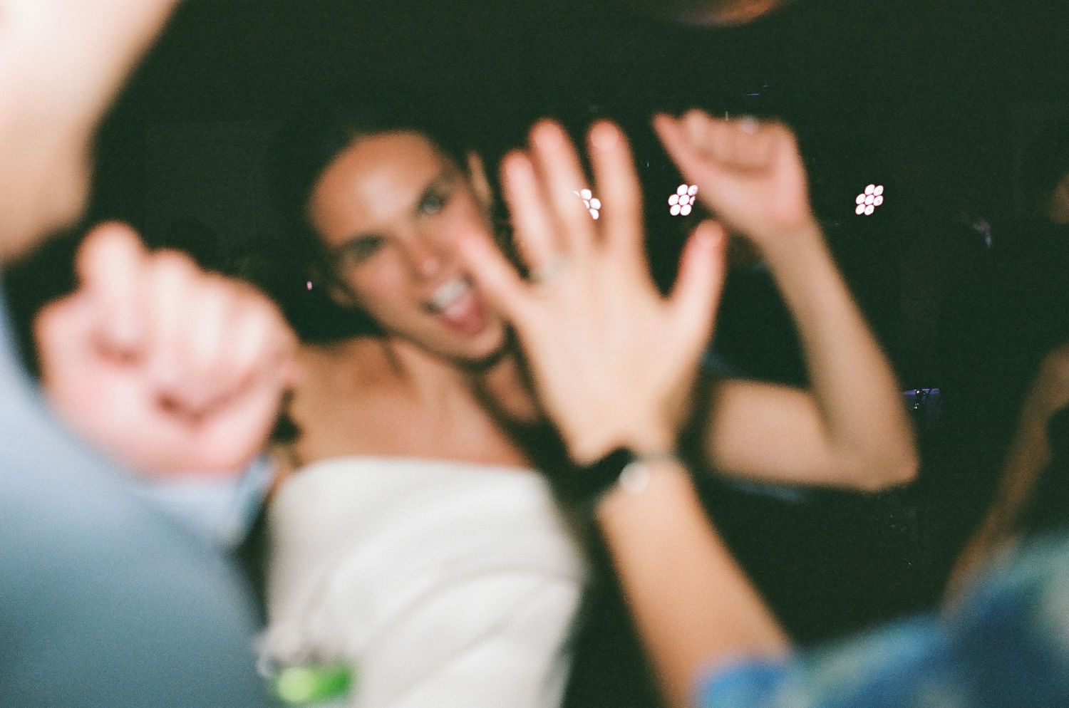 People celebrating at a party with hands raised in the air and dancing on a dark dance floor.