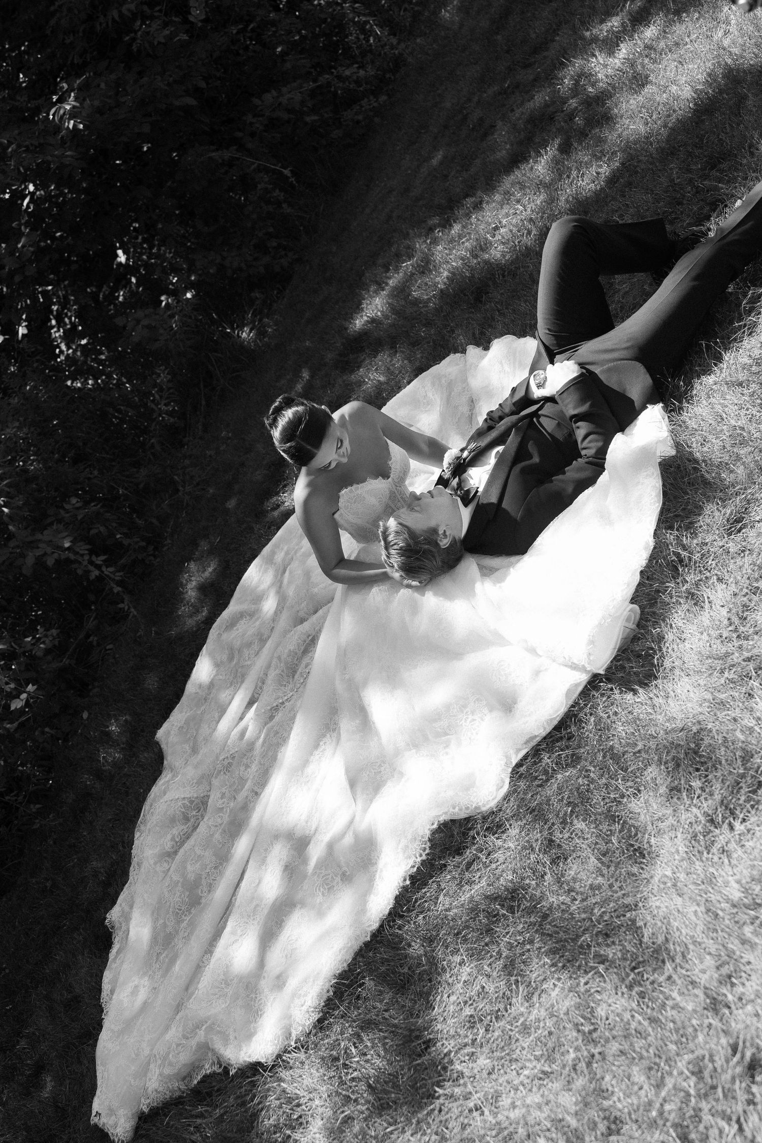 Aerial black and white photo of bride in flowing gown and groom lying on grass in romantic wedding portrait.