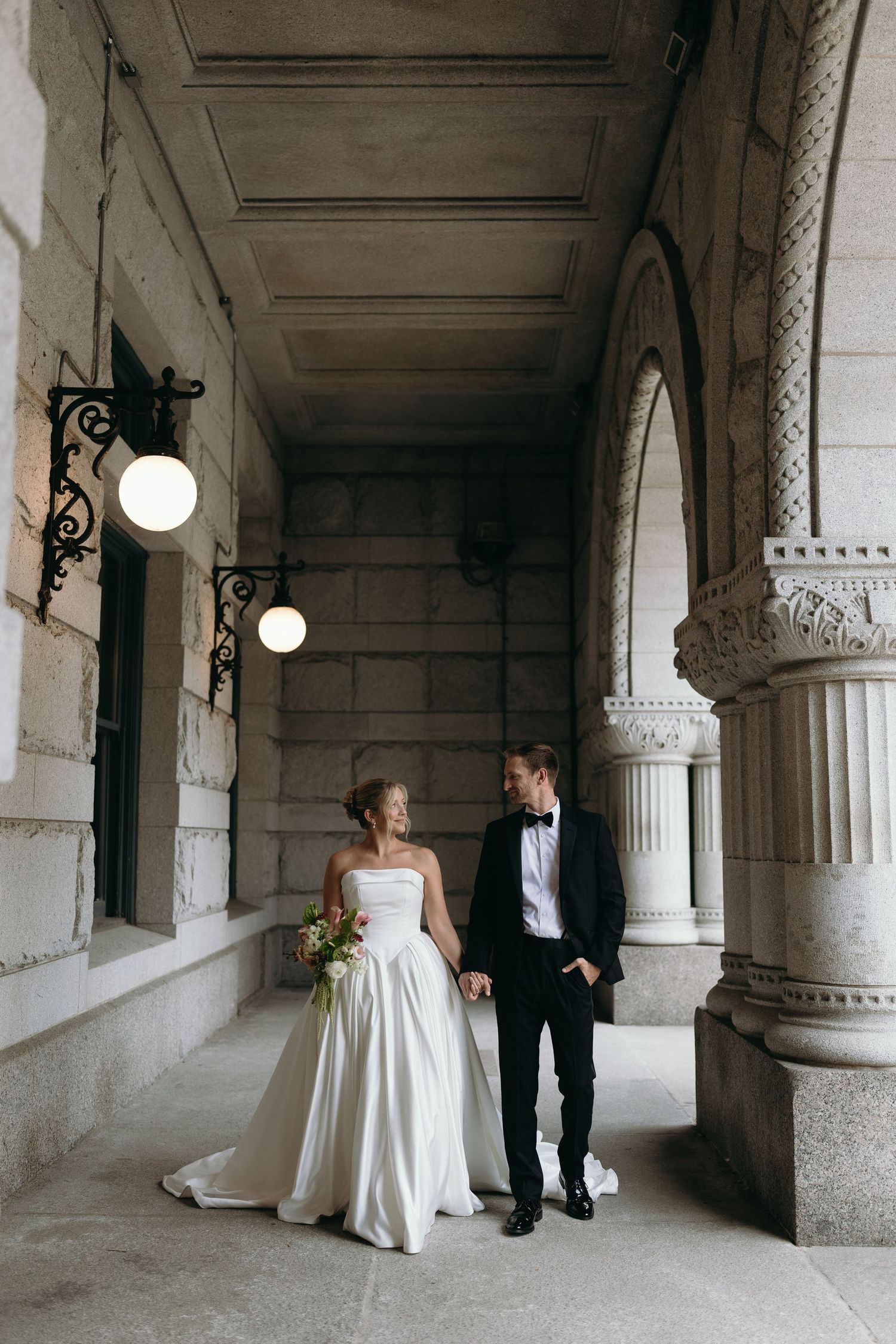A bride and groom share intimate moments in a classic white columned hallway during their wedding photoshoot.