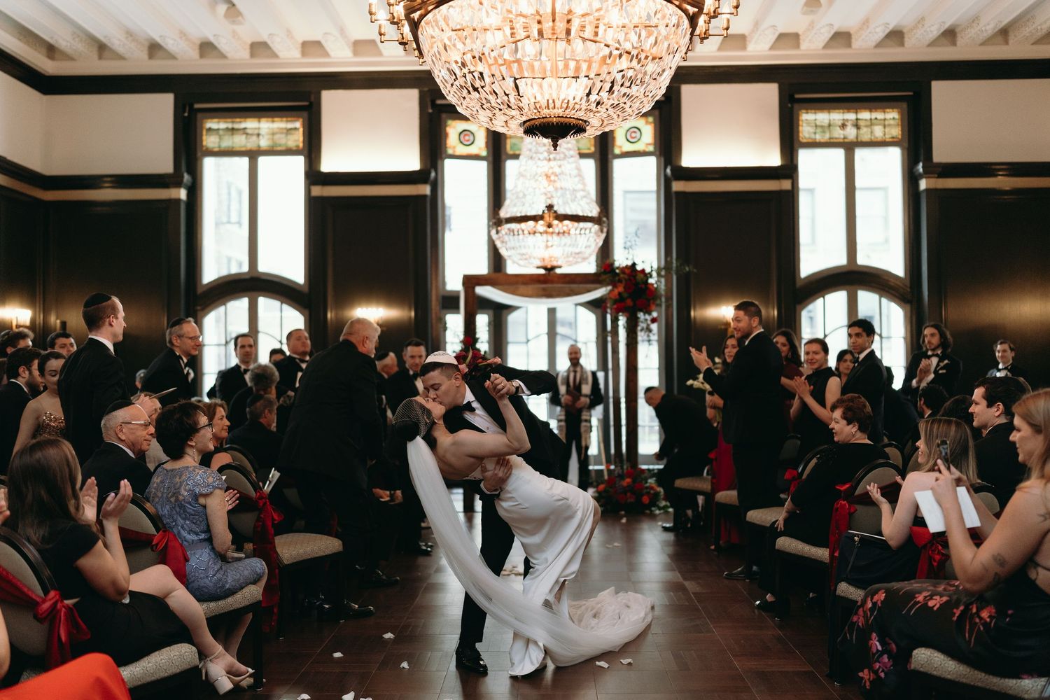 Couples dancing together in an elegant ballroom with crystal chandeliers and large windows.