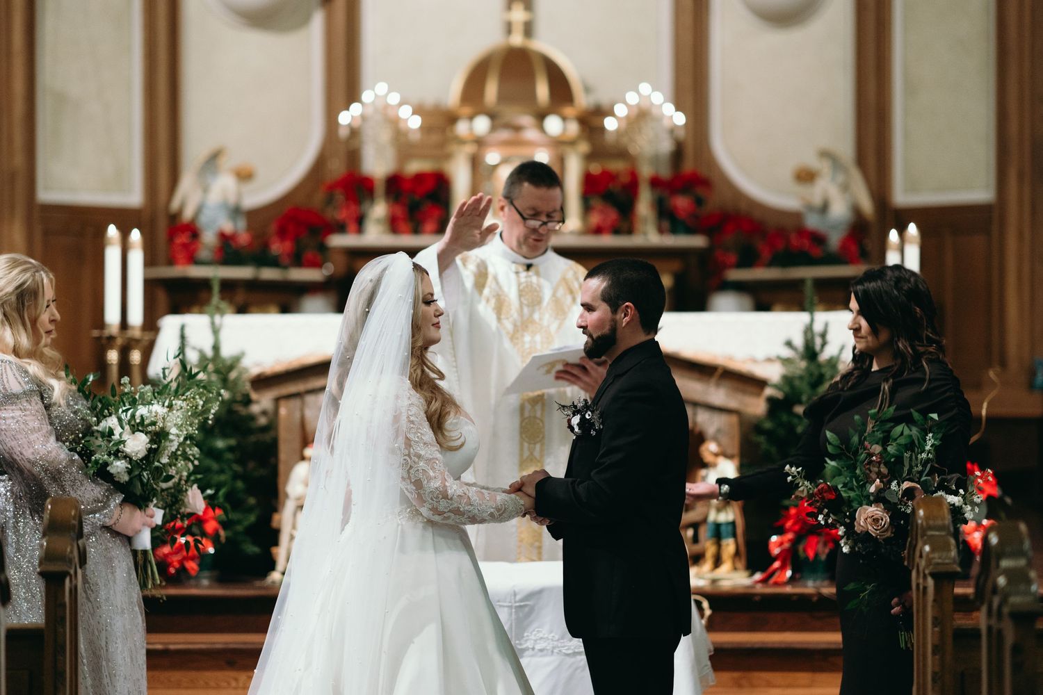 Traditional wedding ceremony being performed at decorated church altar with poinsettias and greenery.