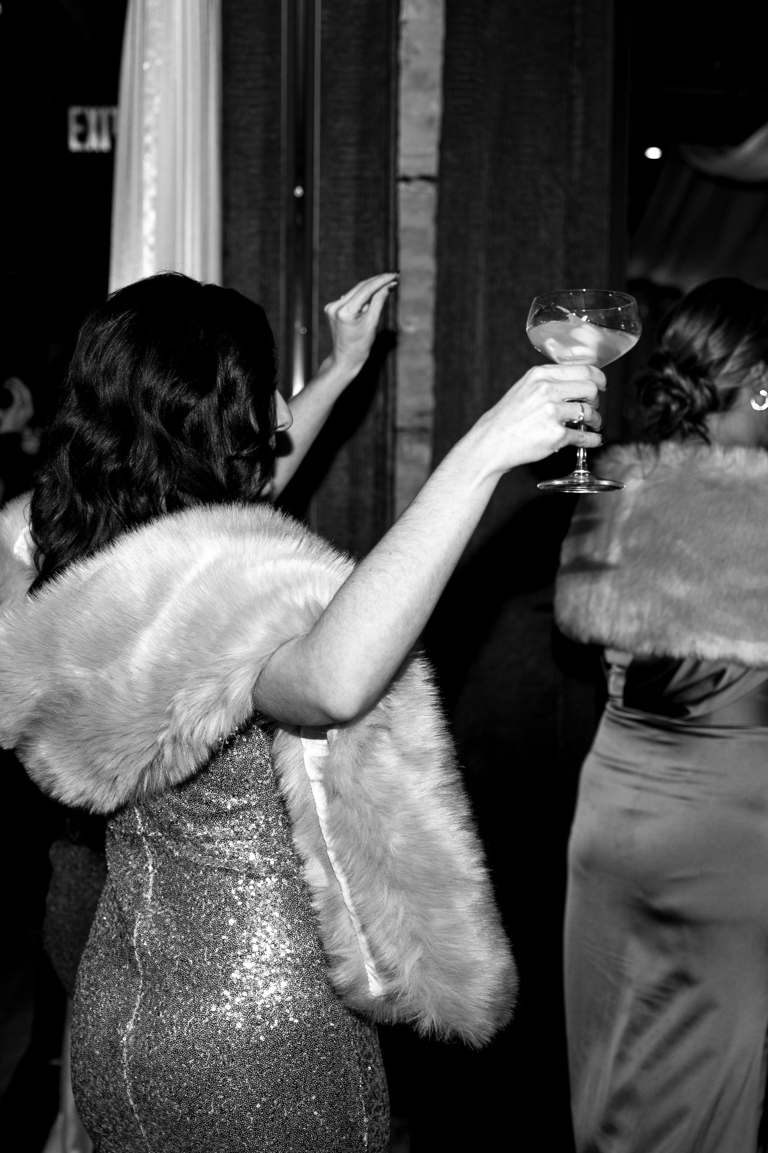 Glamorous party scene with sparkling dresses and raised cocktail glasses in black and white.