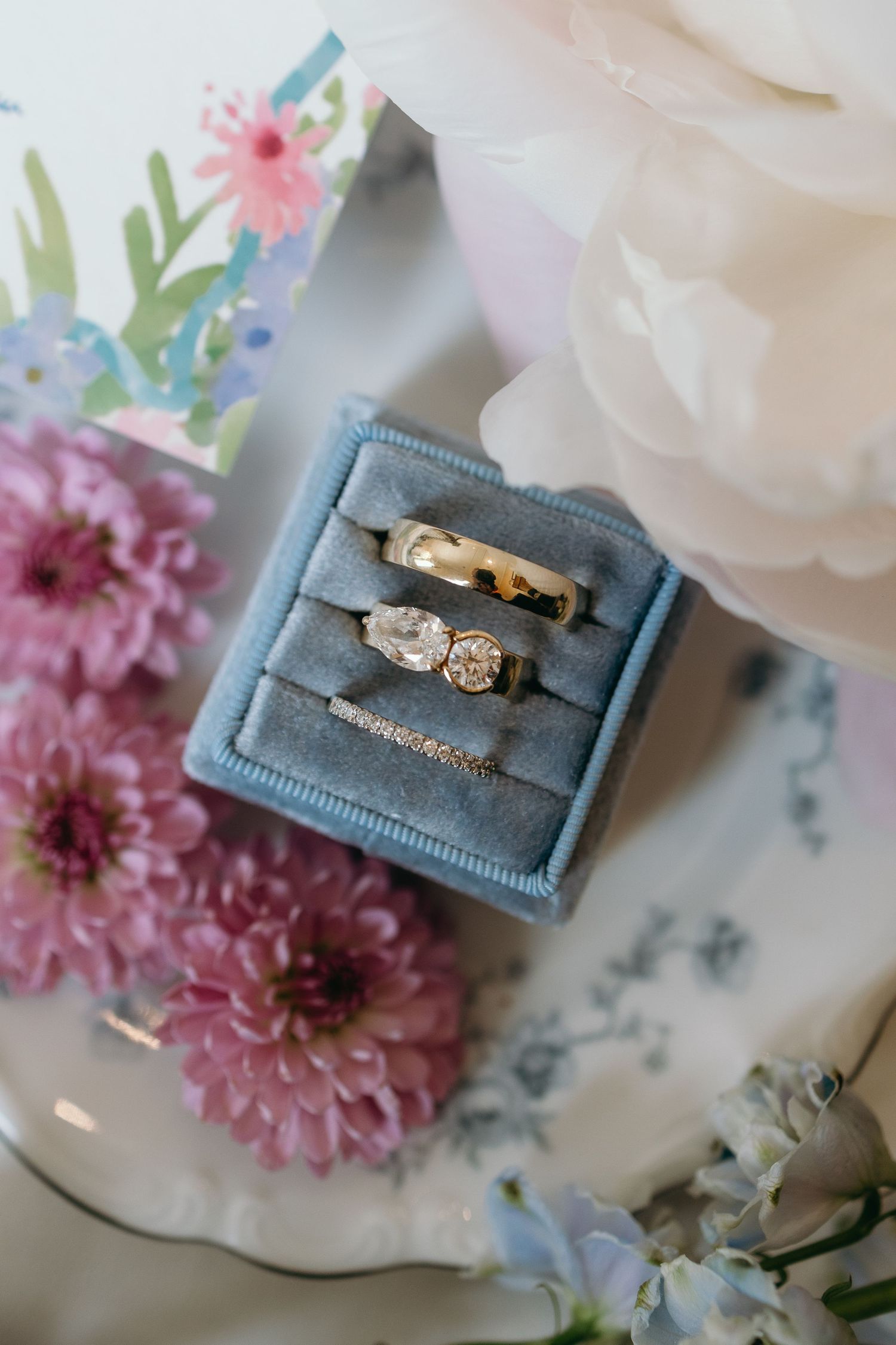 Wedding rings displayed in a blue velvet ring box surrounded by pink dahlias and delicate floral accents. oshkosh wedding photographer