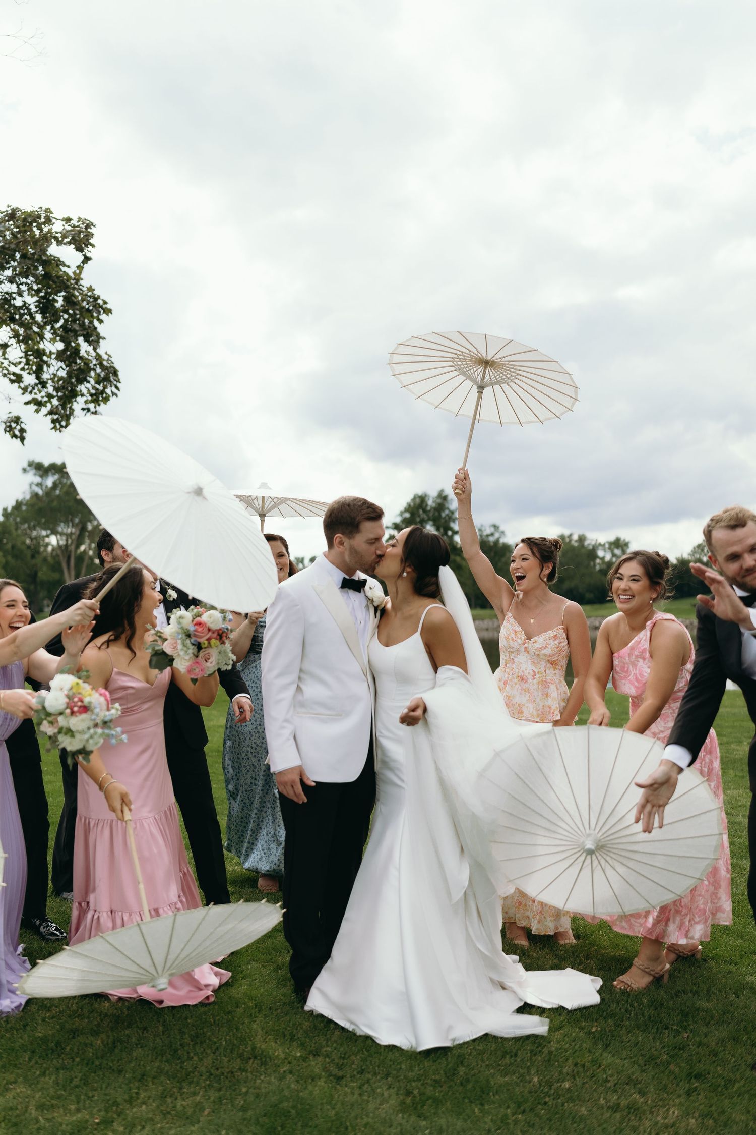 Wedding party celebrates with white parasols on a cloudy day outdoors.