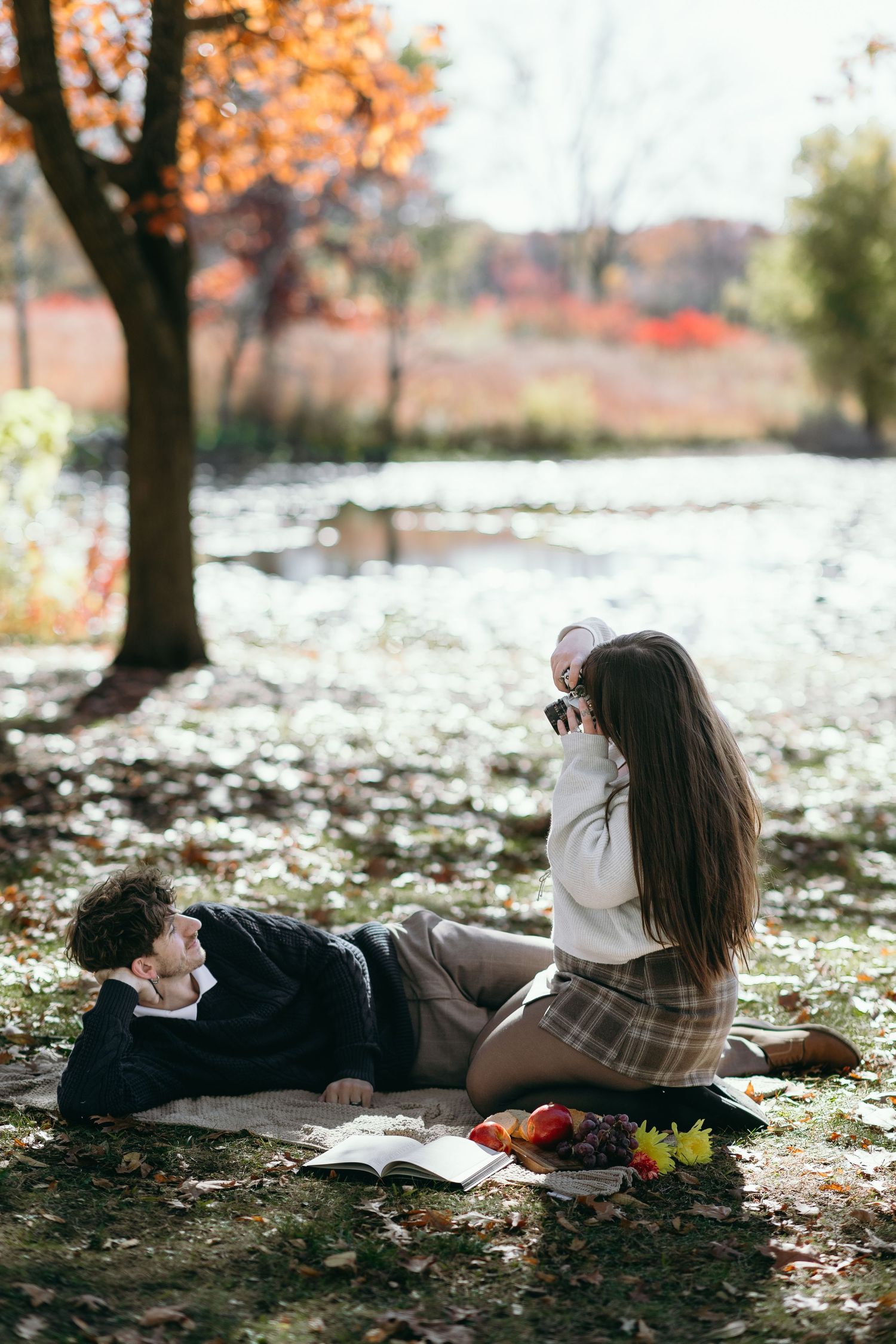 Autumn scene with couple having picnic by pond with fall foliage.