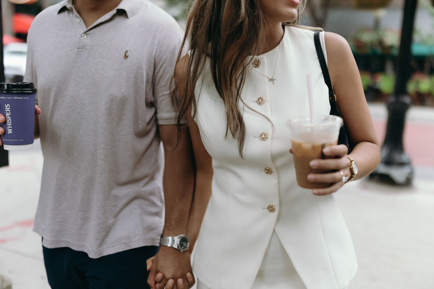 Person in white outfit holding coffee cup while walking on urban street during summer day.