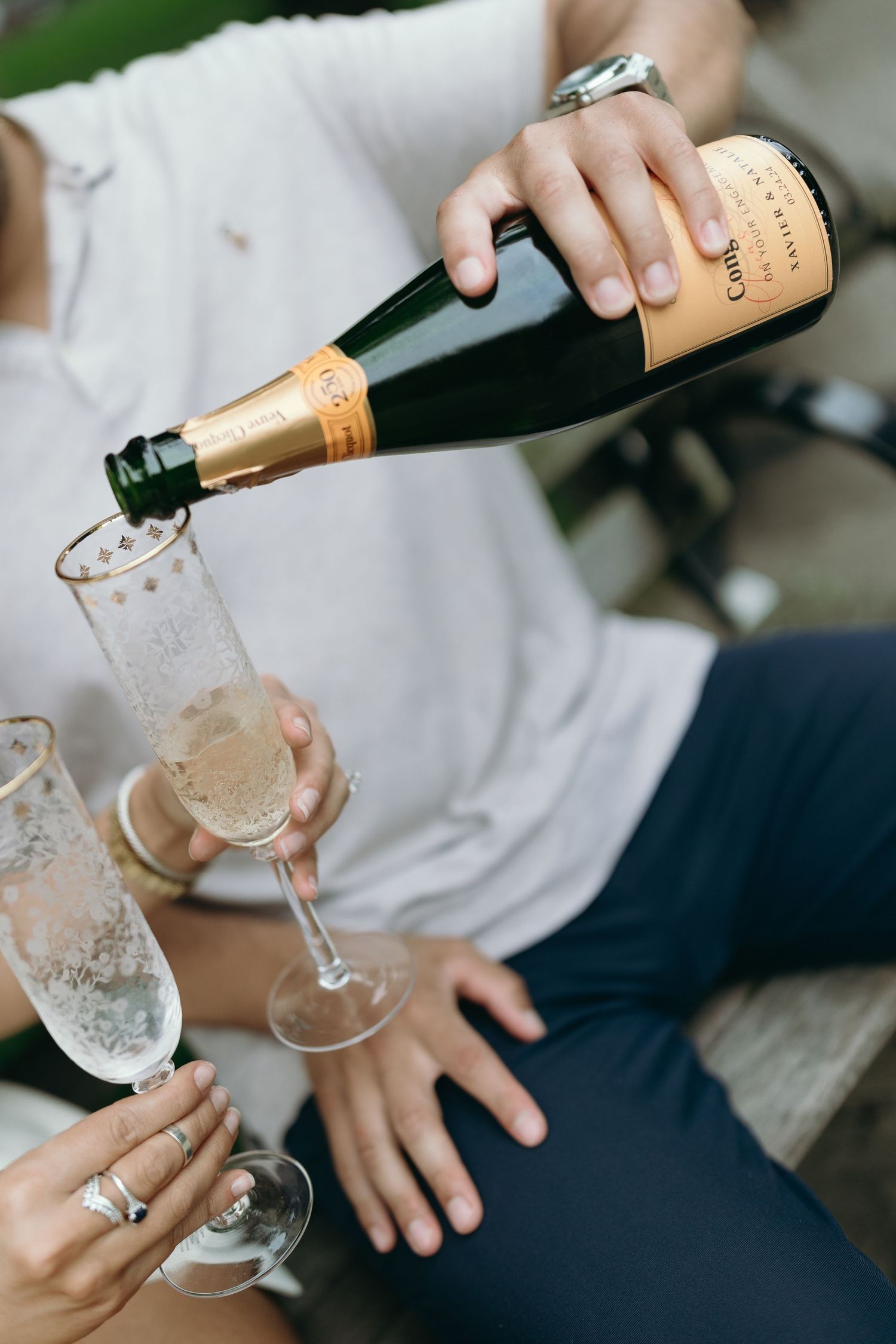 Hands pouring champagne from a bottle into elegant flute glasses in a celebratory setting.