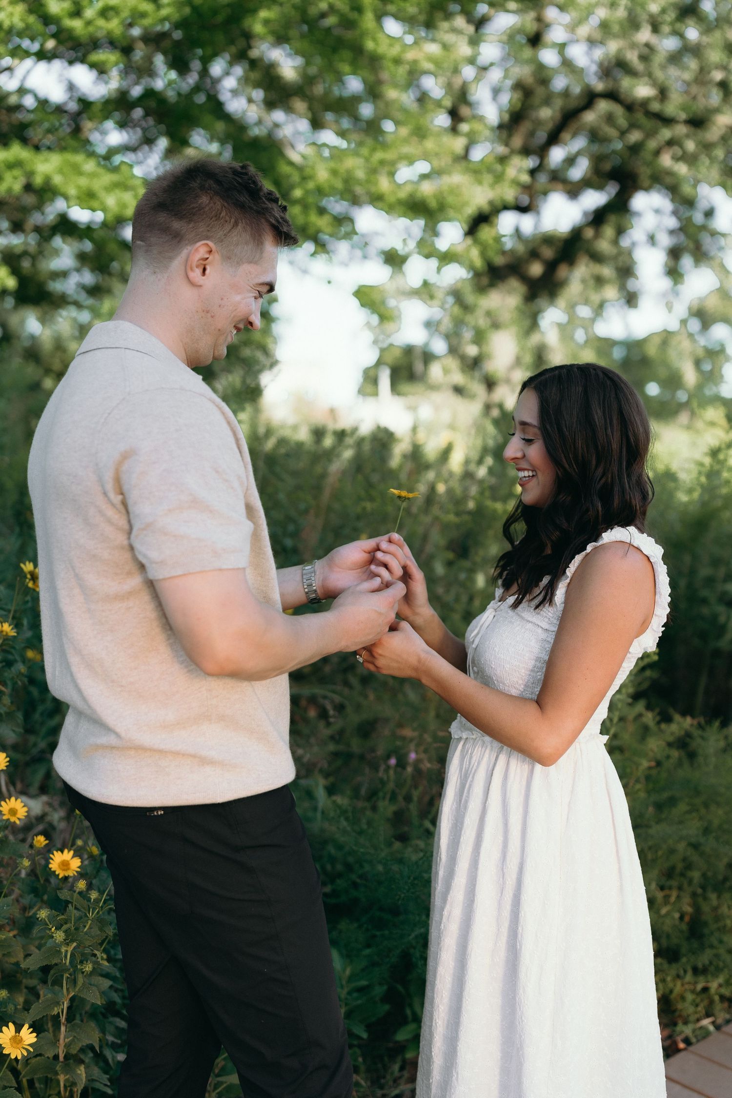 A romantic marriage proposal moment captured in a green outdoor garden setting with wildflowers.