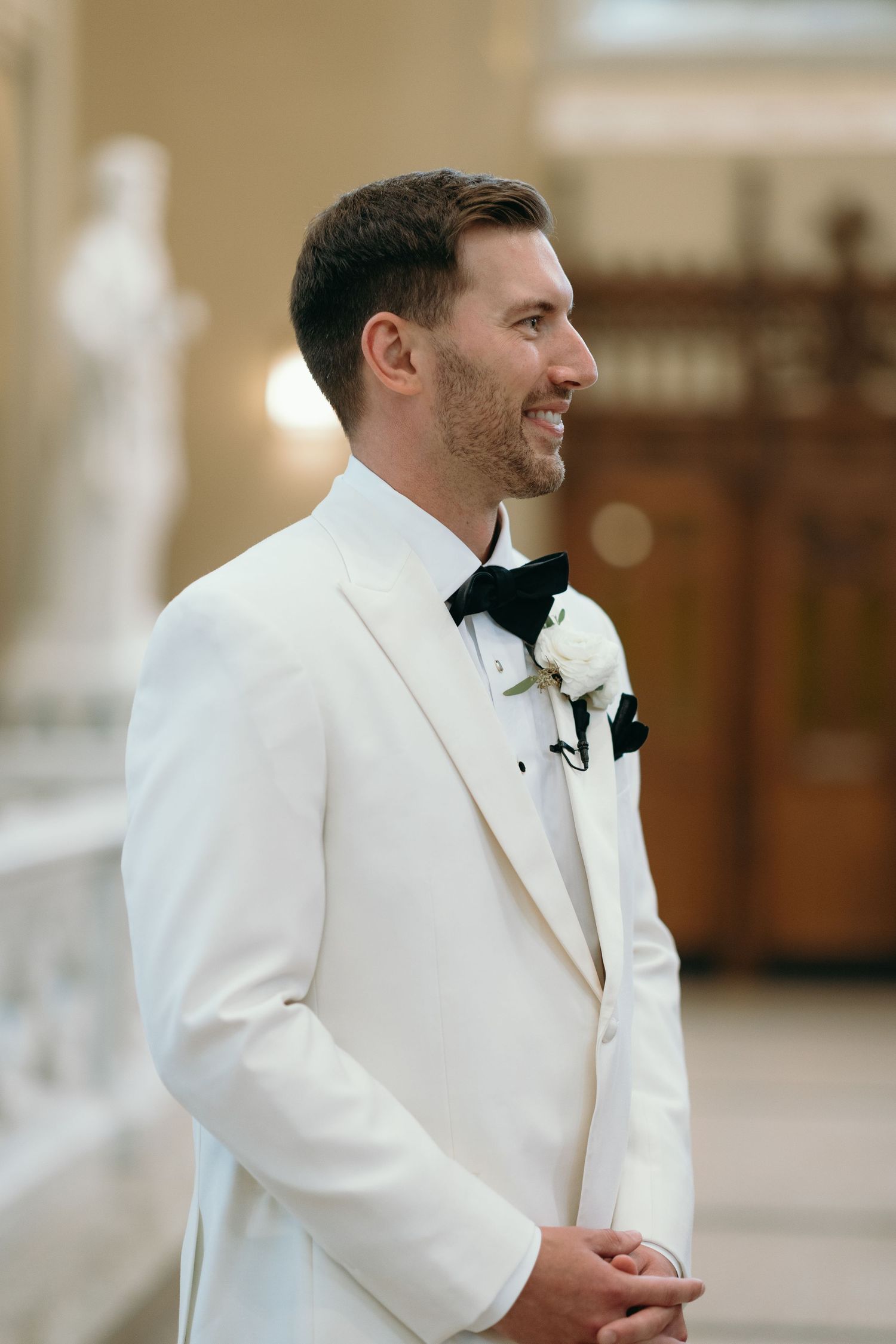 Close-up profile view of groom in white tuxedo jacket with black bowtie.