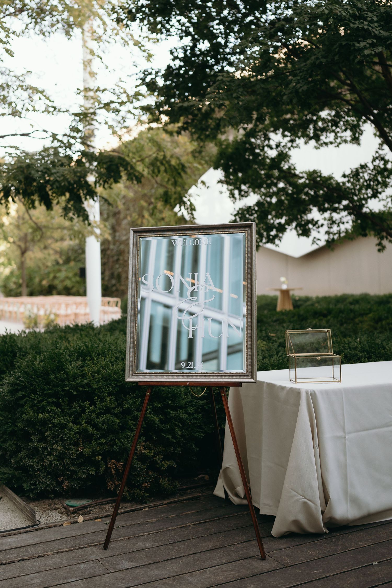 Framed artwork display on wooden easel next to covered table at outdoor event.