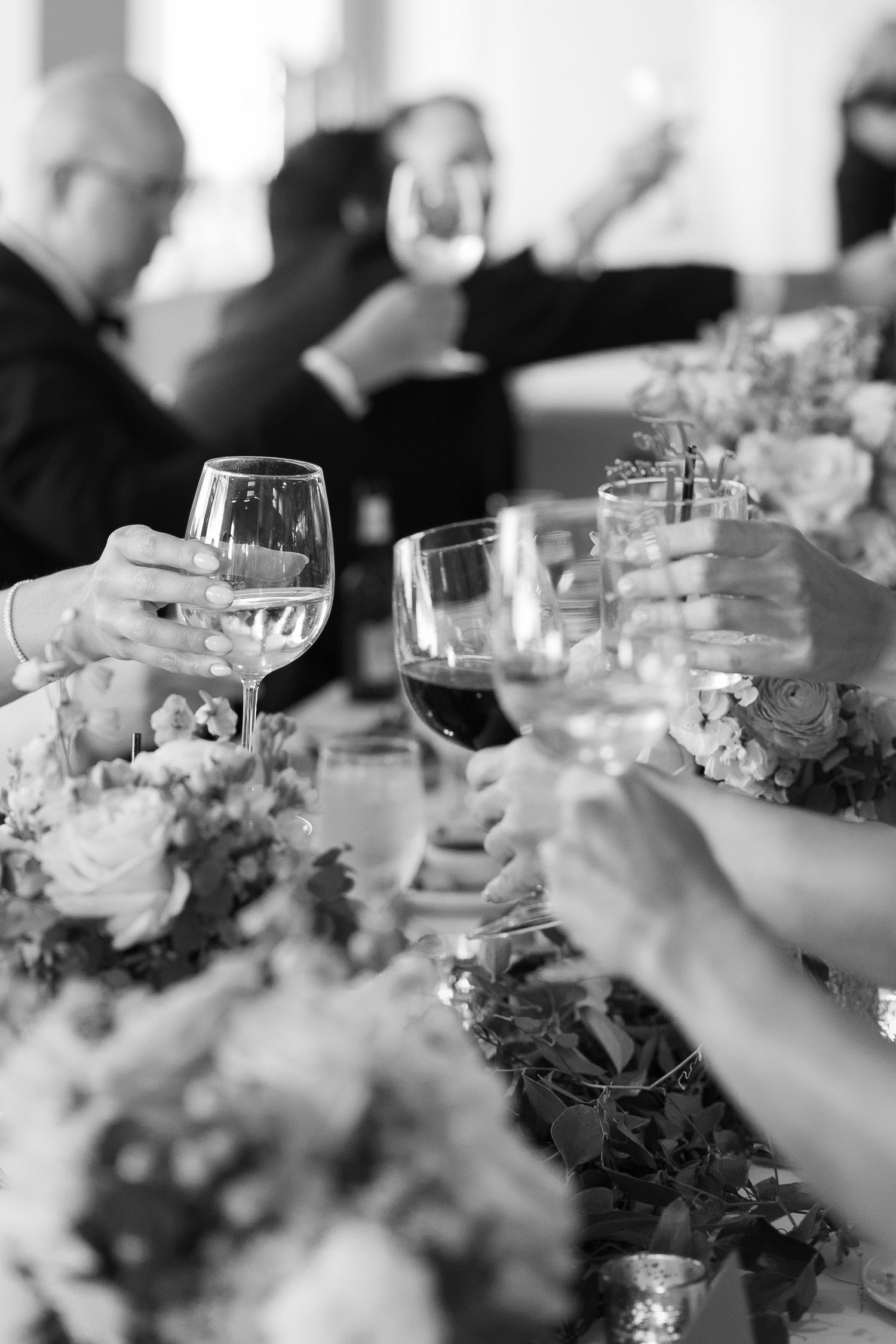 Black and white photo of wine glasses and floral centerpieces at an elegant reception dinner table.