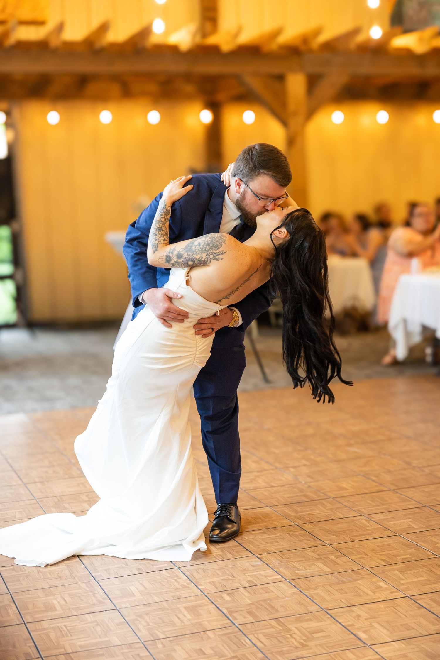 Bride and groom share a romantic dip kiss on the dance floor during their first dance at a rustic barn wedding reception.