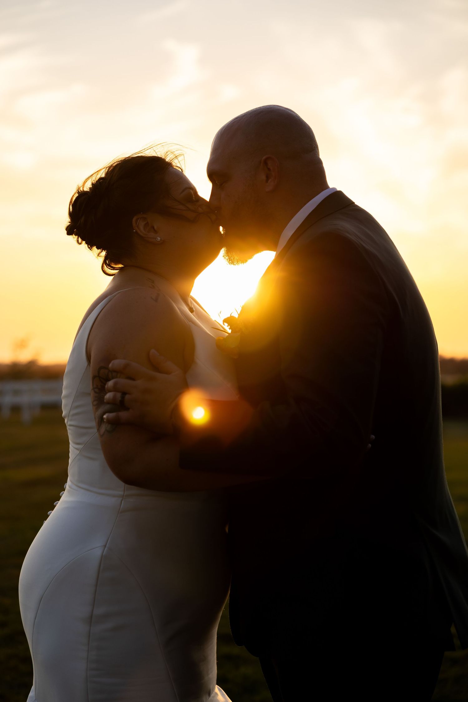 A couple shares a romantic kiss at sunset in a field, creating silhouettes against the golden sky.