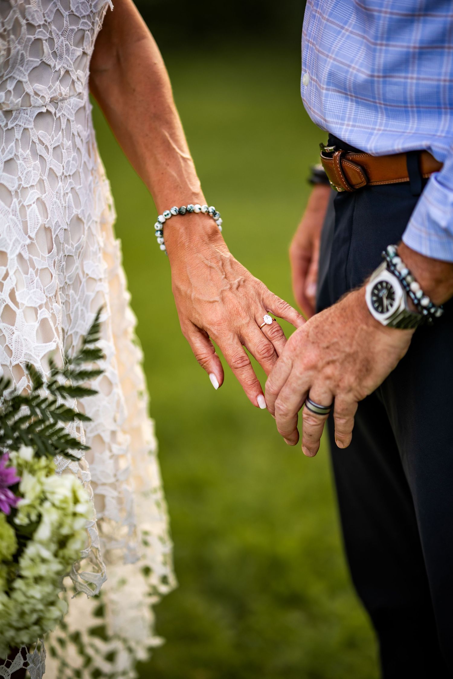 Close-up sequence of hands holding each other against white lace and blue plaid clothing in an outdoor setting.